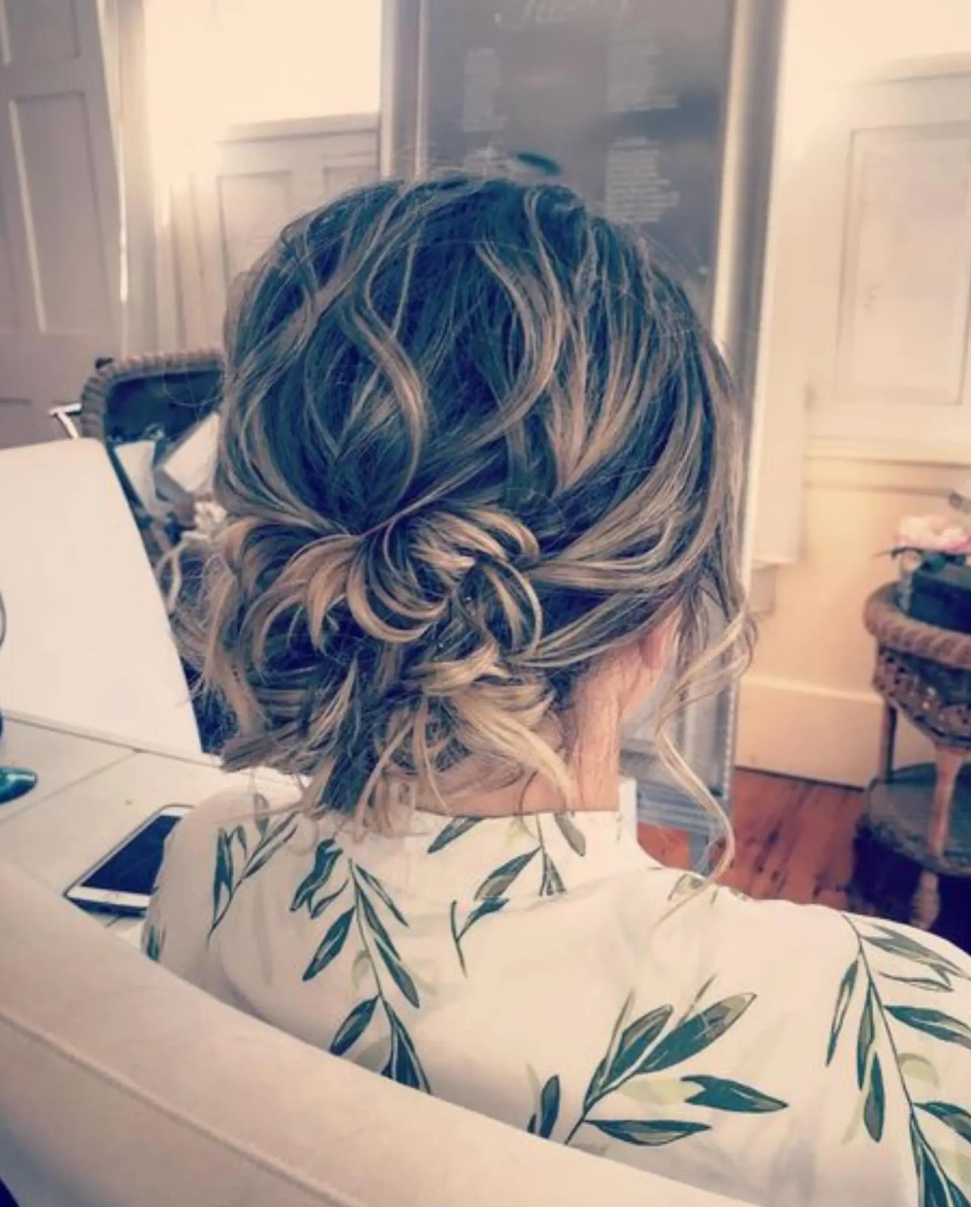 A textured and voluminous low updo with soft curls gathered into an effortless chignon, highlighted by multi-tonal dimensional color. 1