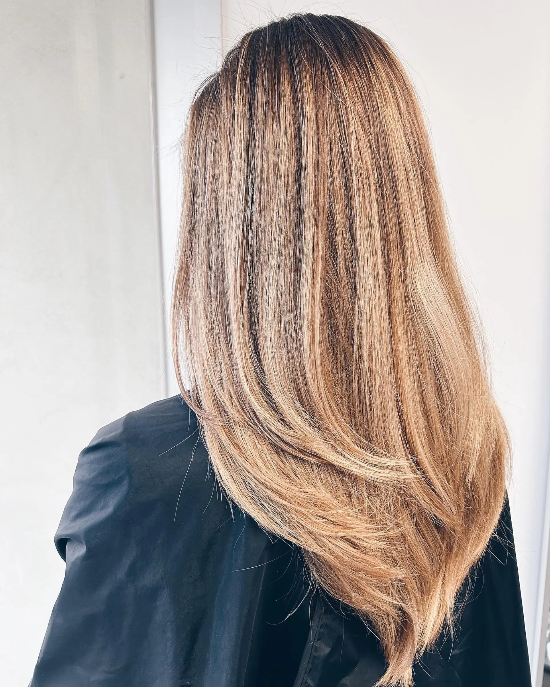 Long straight hair featuring feathered V-shaped layers and a multi-dimensional warm honey blonde balayage. 1