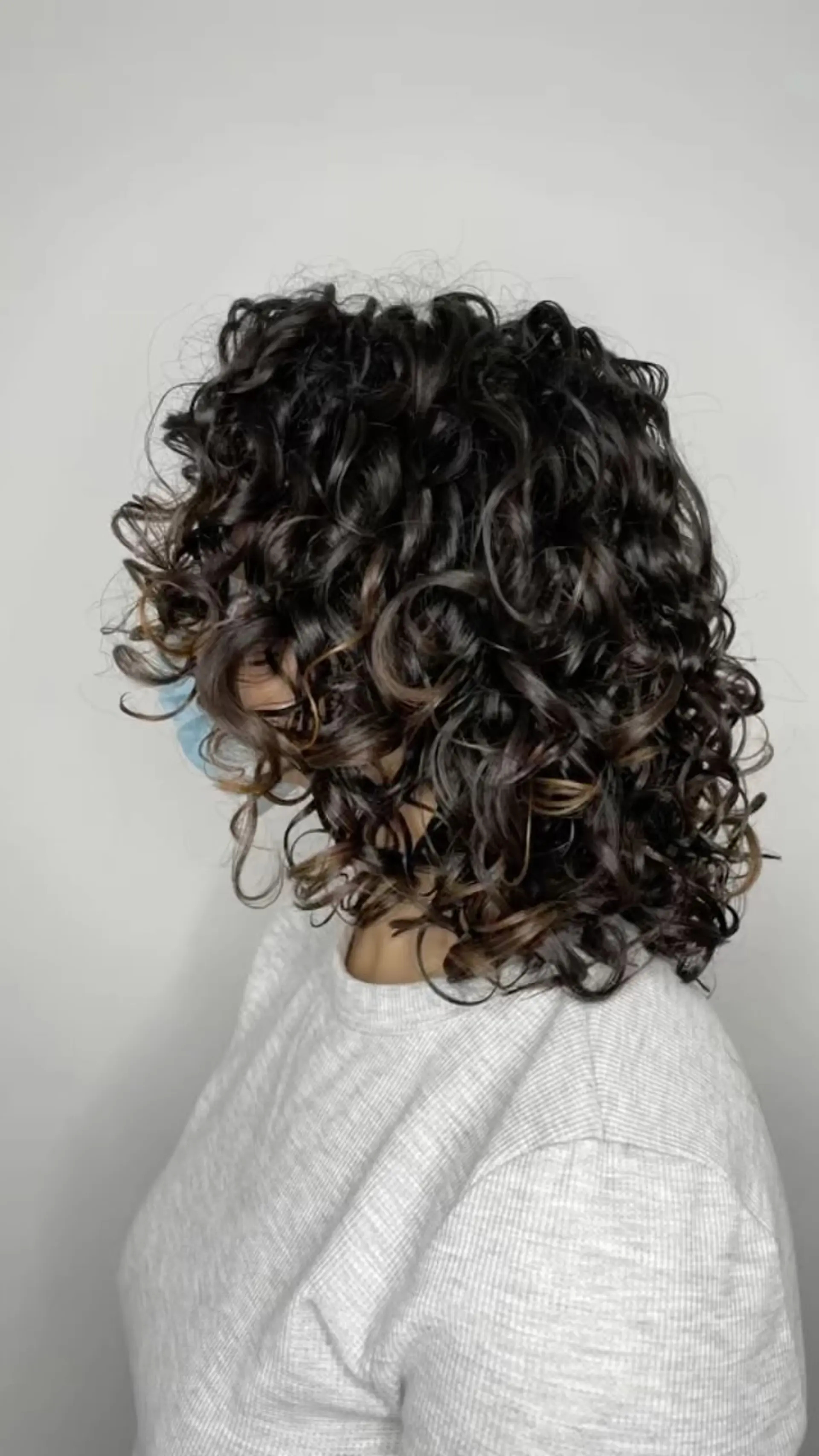 A medium-length layered cut styled with bouncy, glossy, well-defined curls and subtle dimensional highlights. 1