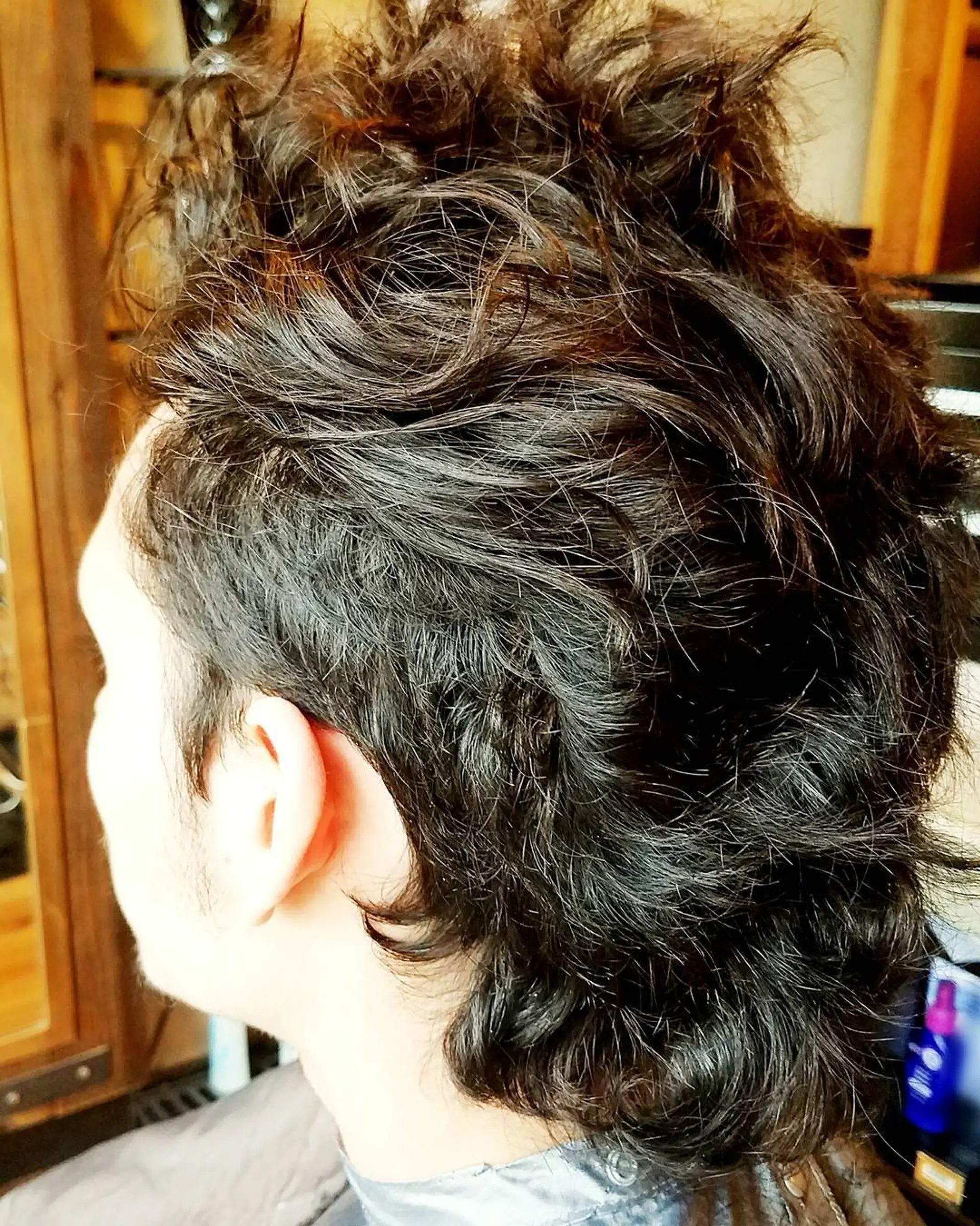A textured modern mullet featuring tapered sides with voluminous, messy waves through the crown and nape. 1