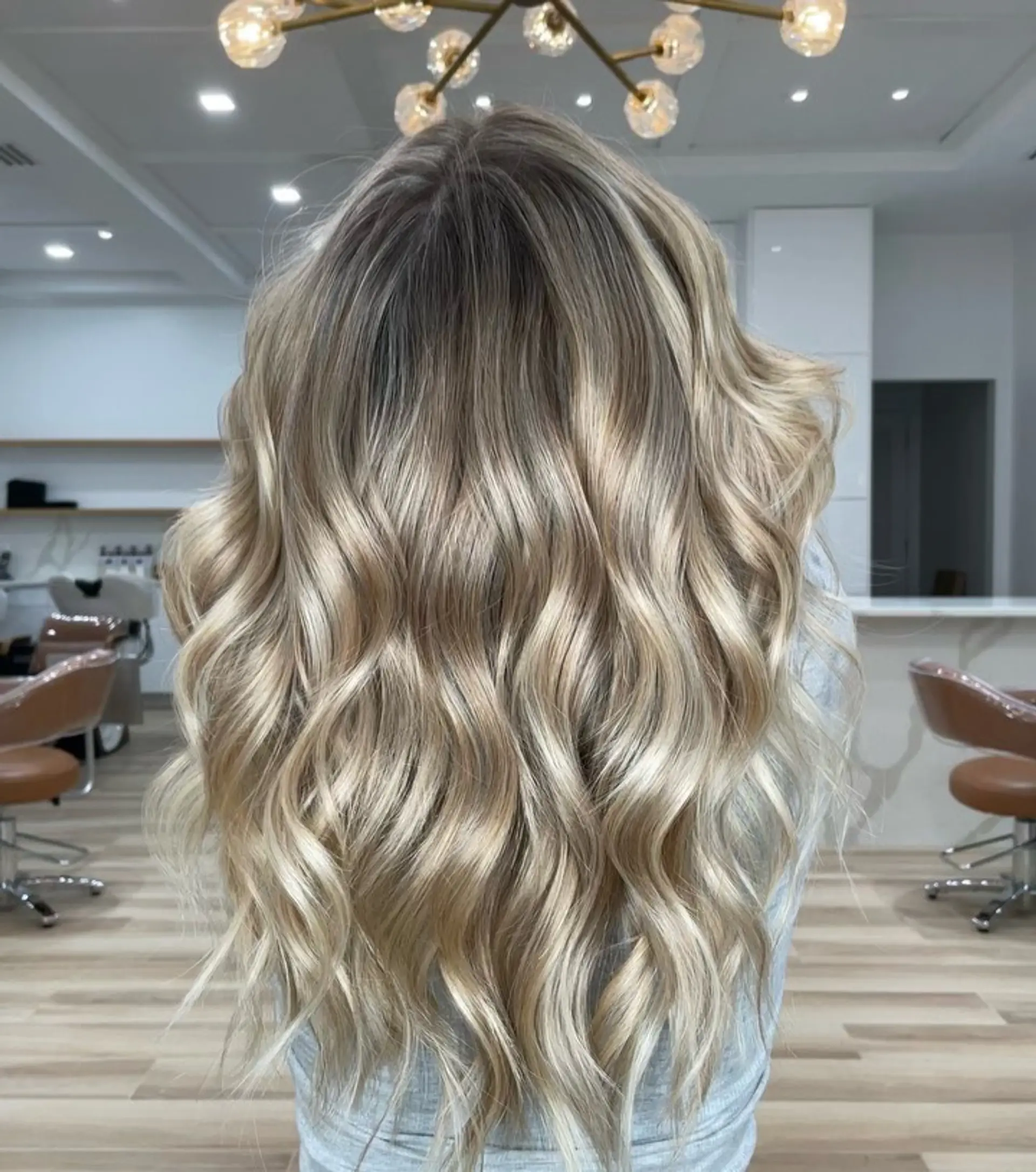 Long dimensional blonde hair styled in soft, glossy, lived-in waves with a natural rooted effect. 1