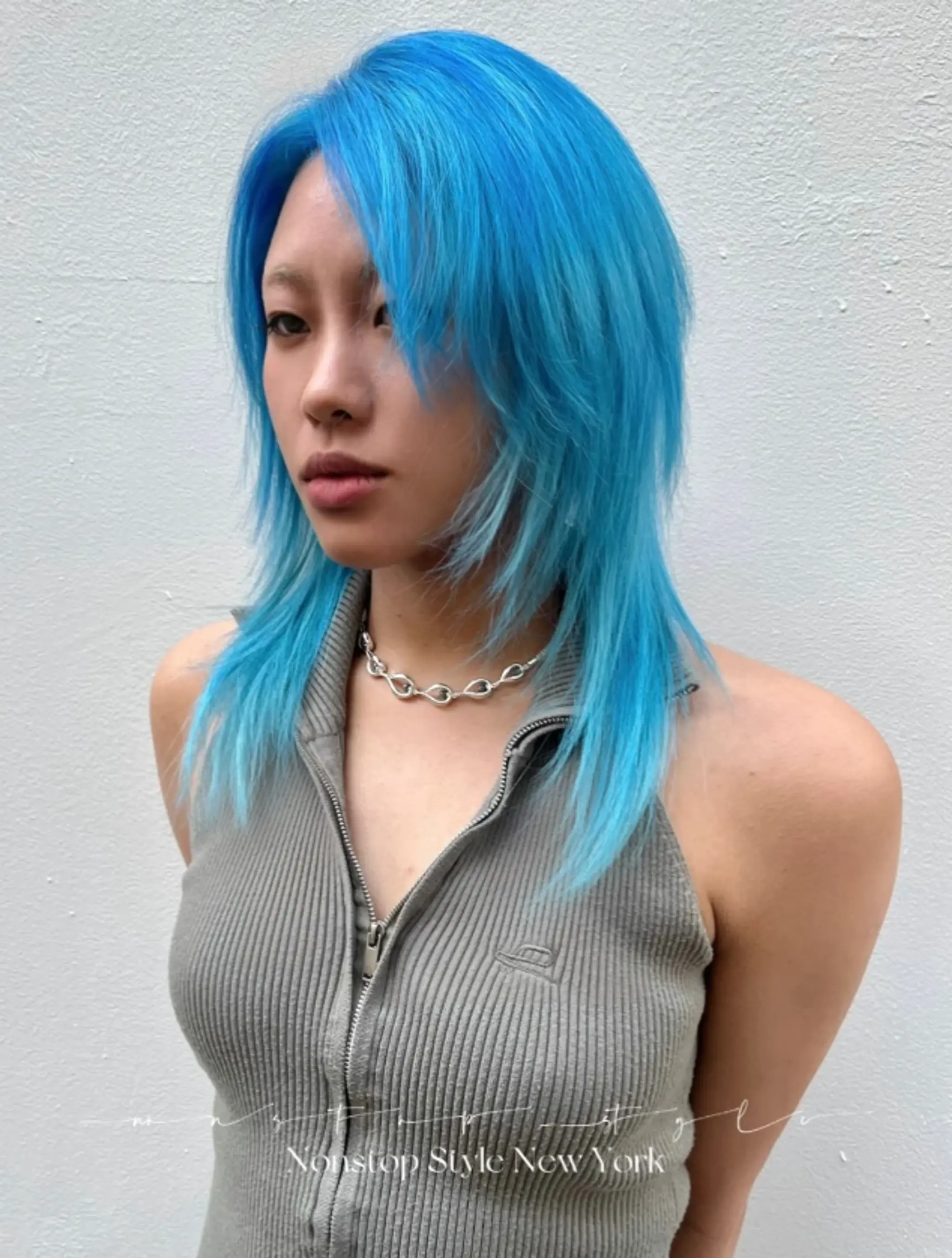 The vibrant electric blue hairstyle features straight, medium-length hair styled into a shag cut with multiple layers. The layers frame the face and add volume, with feathered ends and a slight side part for a stylish, edgy look.
(NonstopStyle: by Neil)