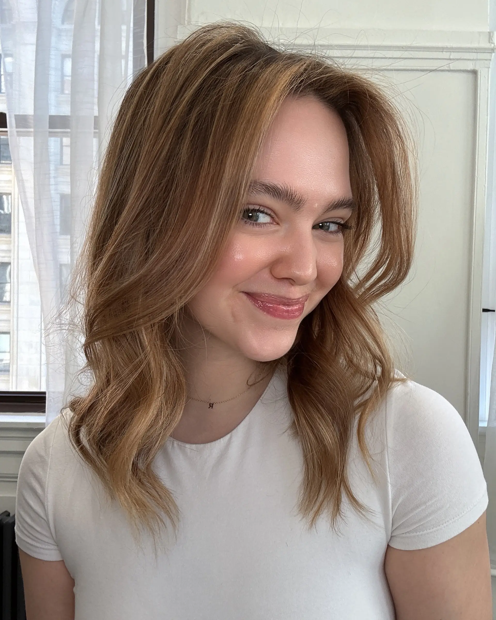 A collarbone-length cut with face-framing curtain layers, styled in soft waves and colored with a seamless bronde balayage. 1