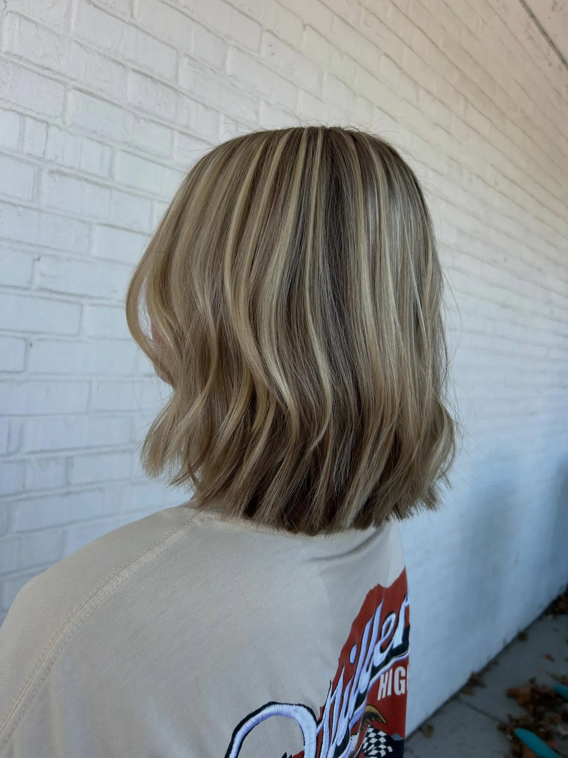 A textured blunt lob cut hitting just above the shoulders, enhanced with bright dimensional blonde highlights and soft wave bends. 1
