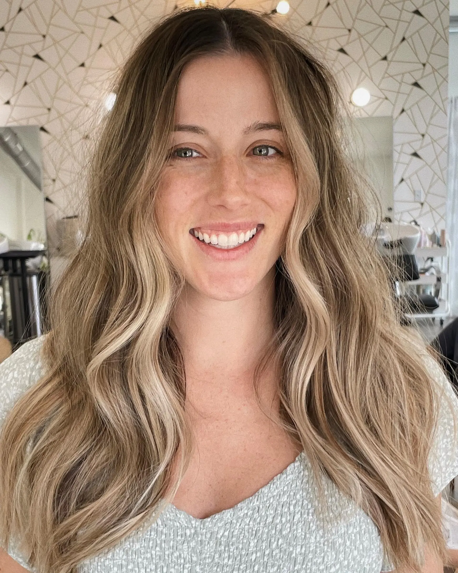 Long hair styled in soft, undone waves featuring dimensional blonde balayage with face-framing highlights. 1