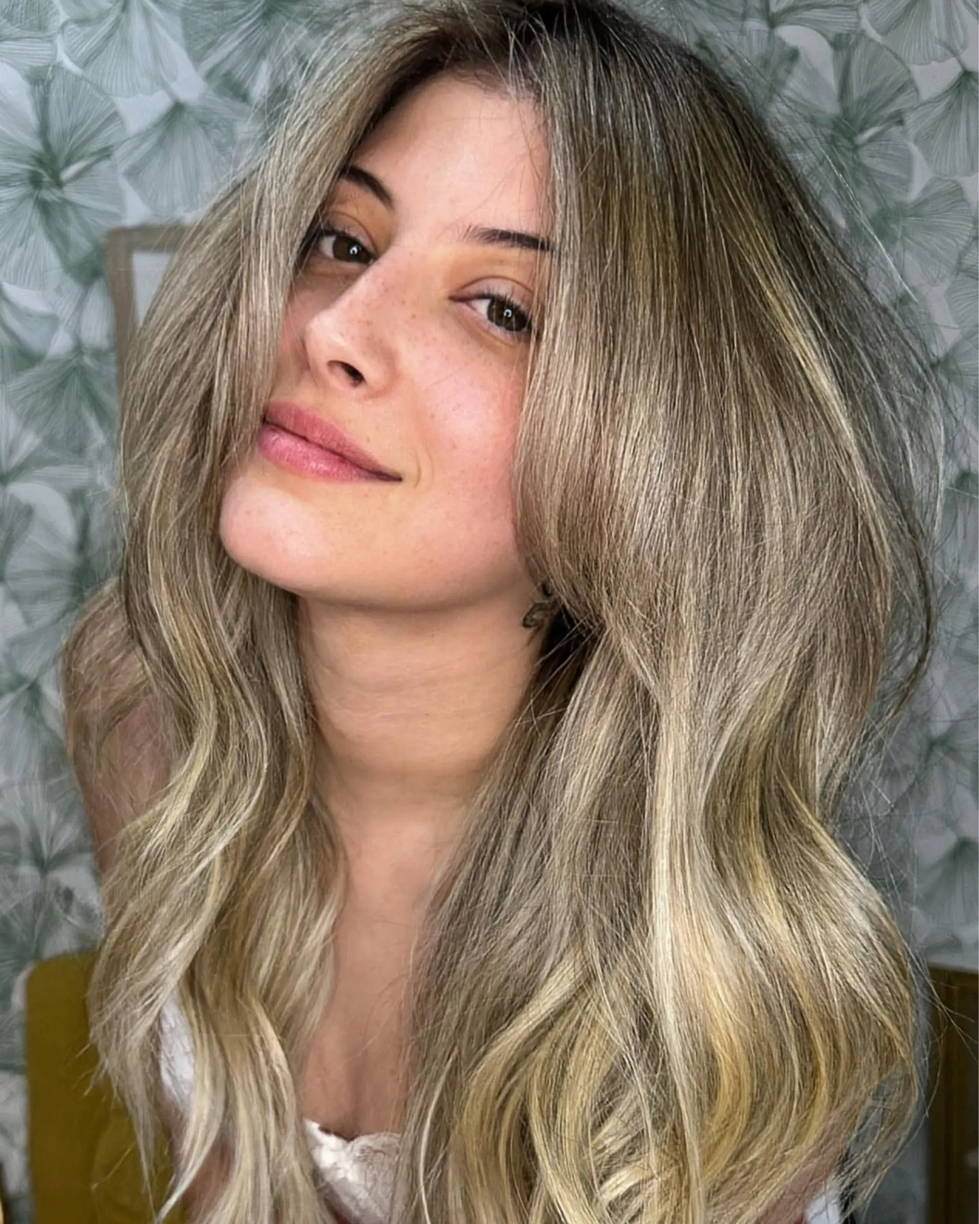 Long, dimensional ash blonde hair styled into soft blowout waves with voluminous curtain bangs. 1