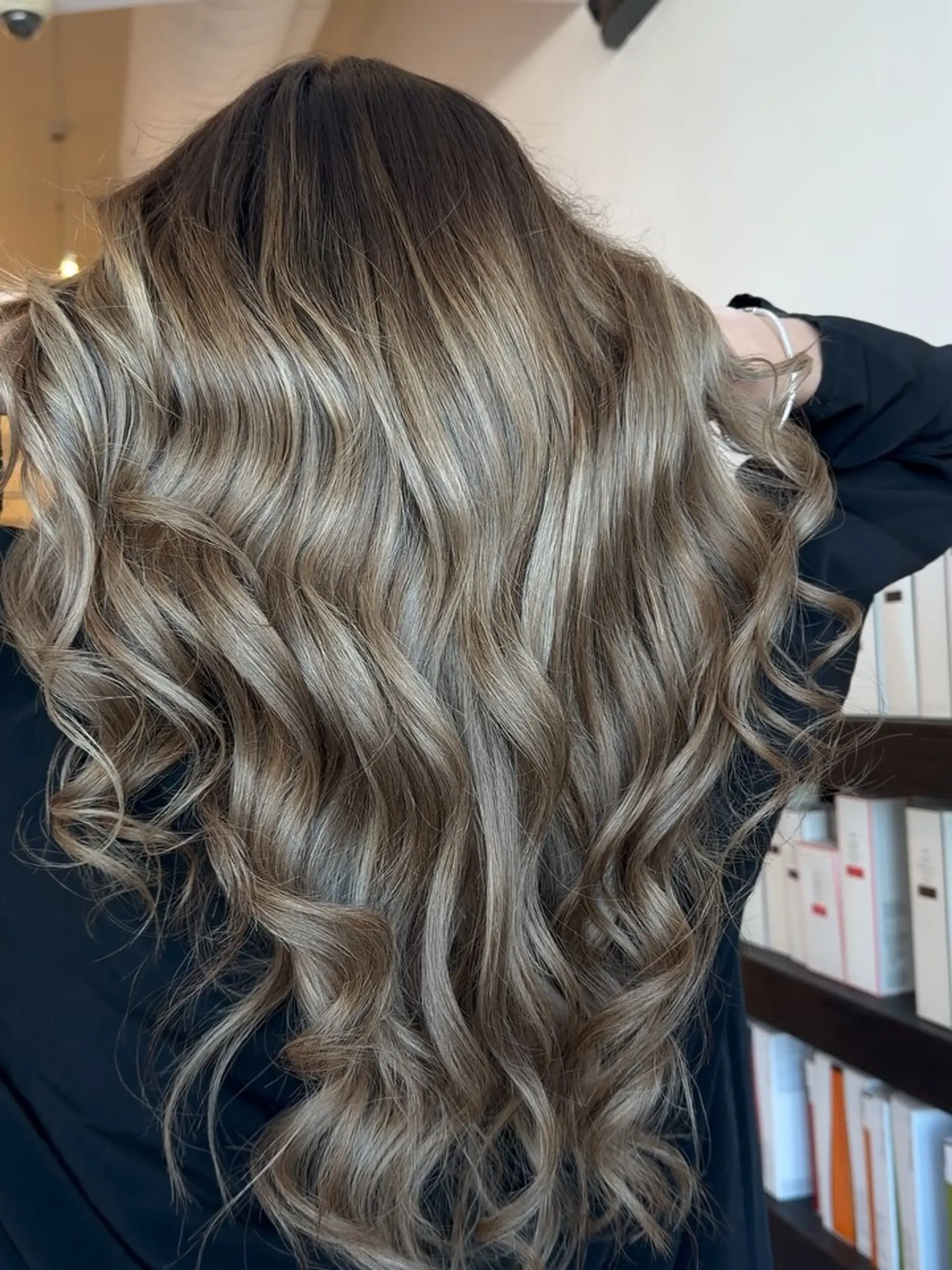 Cool-toned bronde balayage with dark blended roots cascading into soft ash blonde ribbons and loose waves. 1