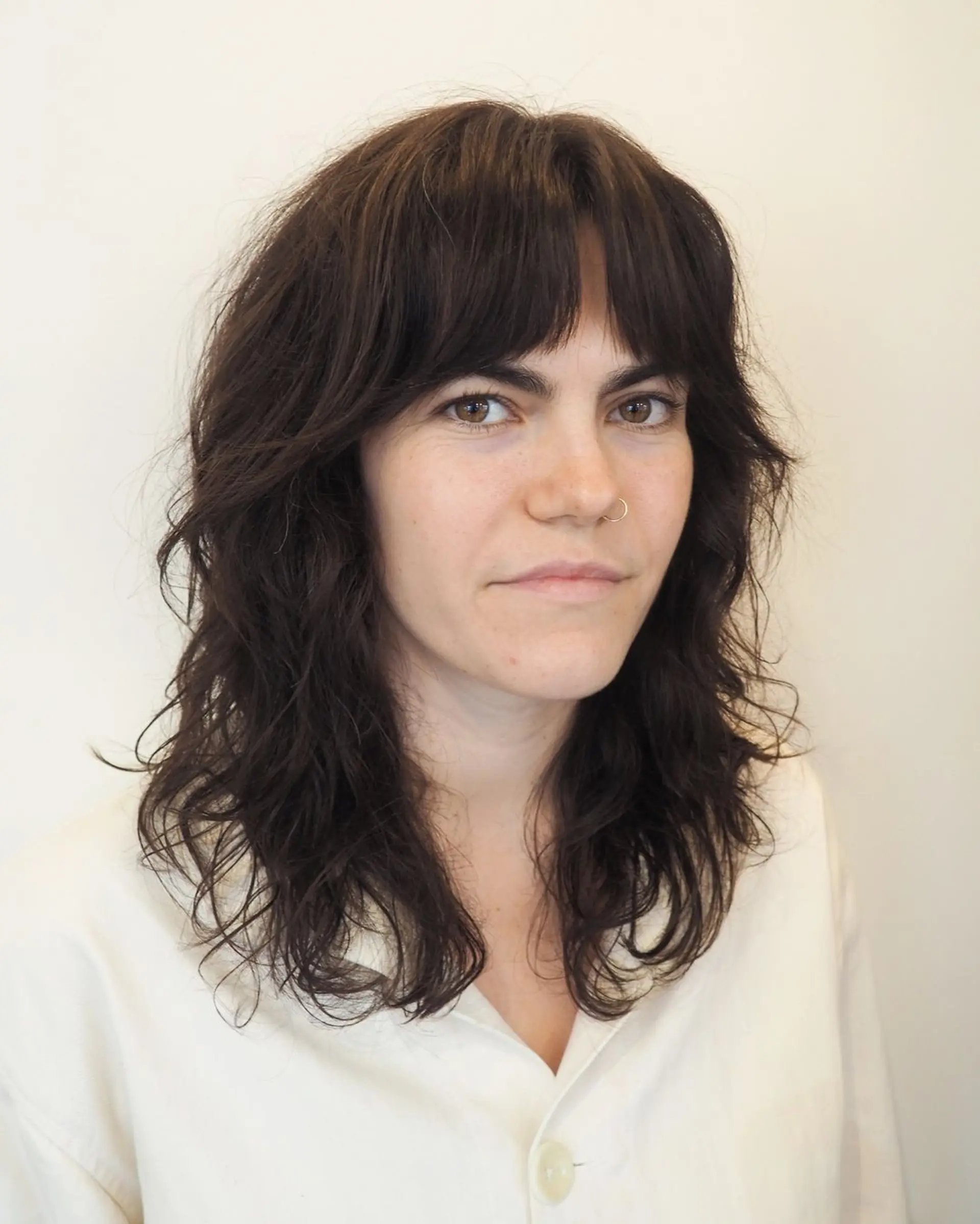 Medium-length, dark brown waves with a soft, natural look, featuring textured layers and bangs for a chic, relaxed style. 1