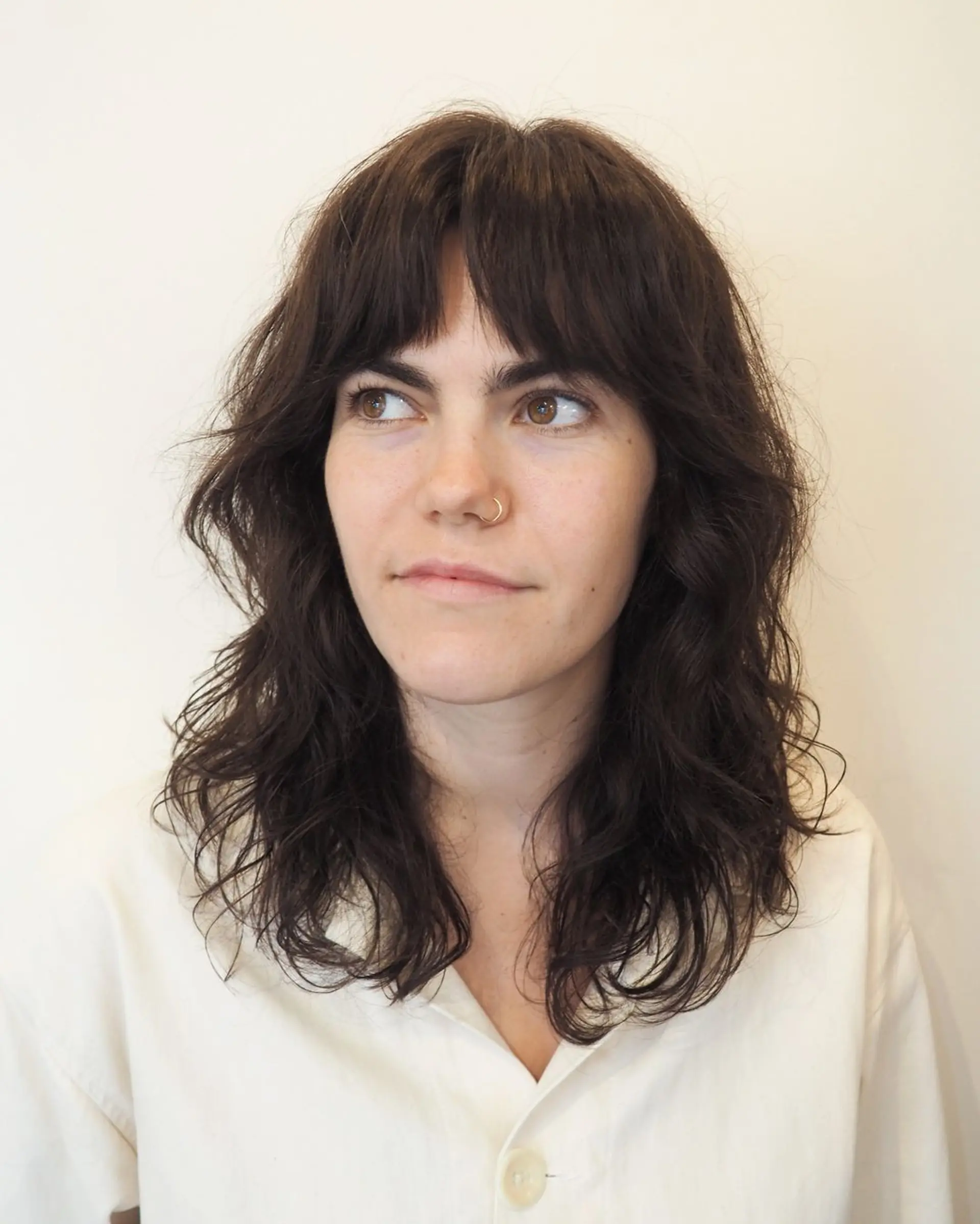 Medium-length, dark brown waves with a soft, natural look, featuring textured layers and bangs for a chic, relaxed style. 2