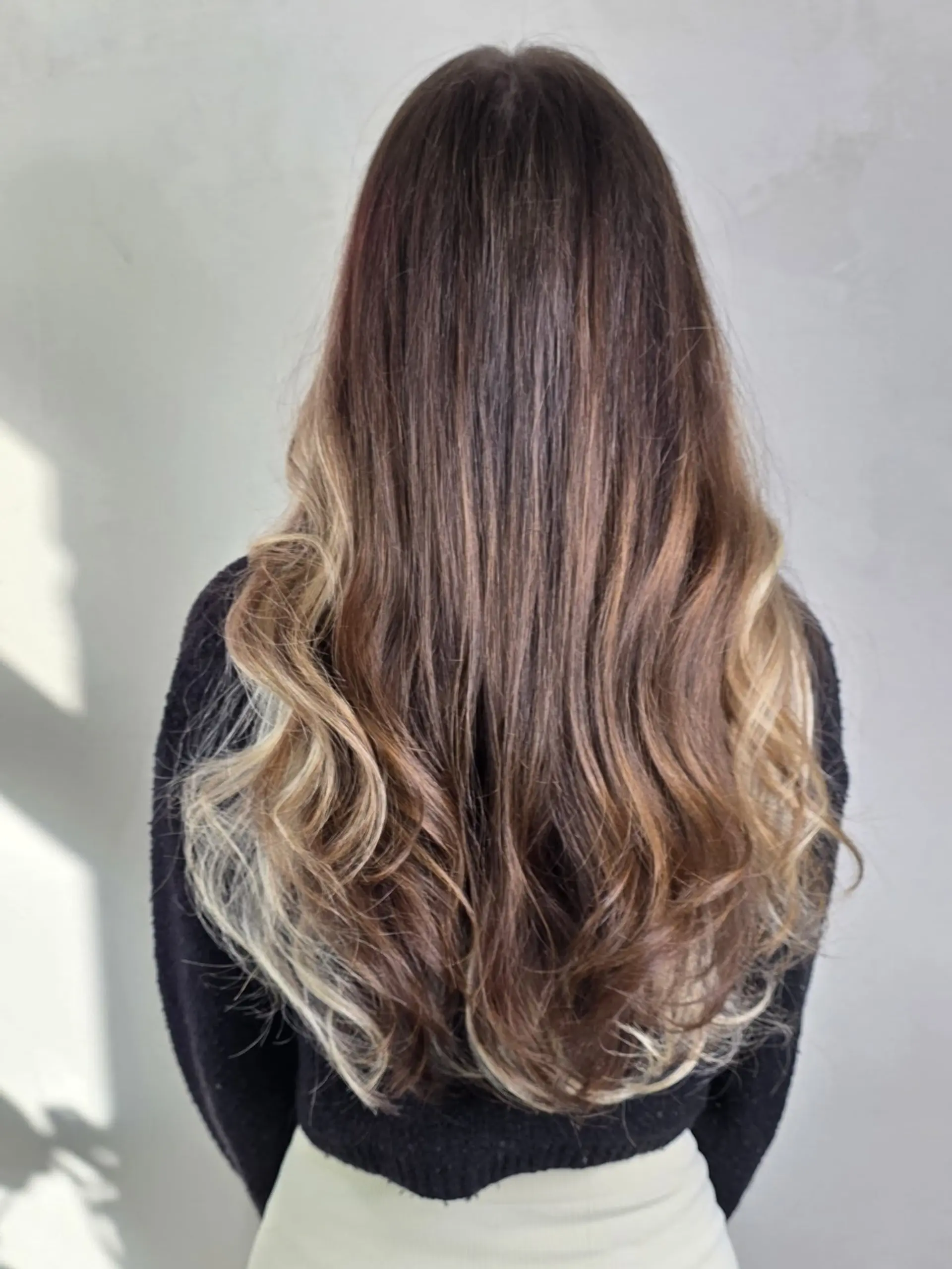 Long brown hair styled in soft waves with contrasting blonde halo highlights placed along the underneath layers. 1