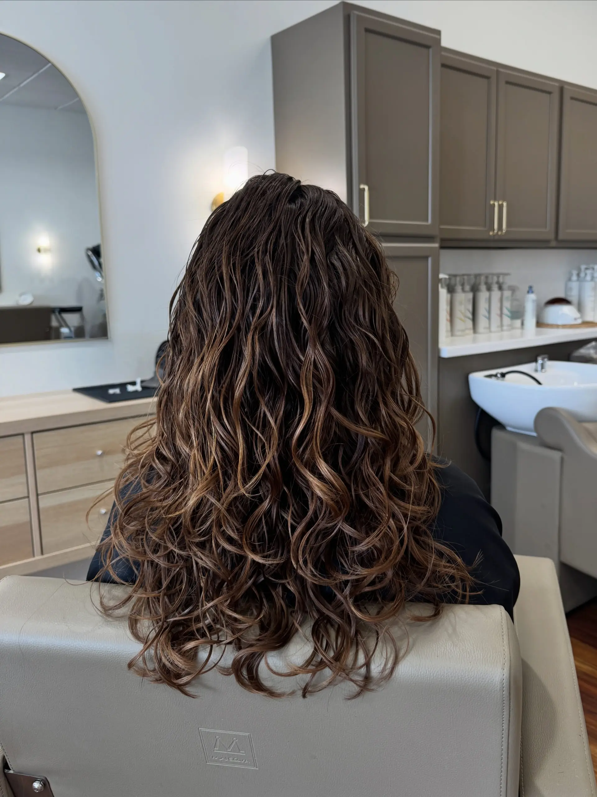 Long, defined brunette curls styled to accentuate natural texture and dimension. 1