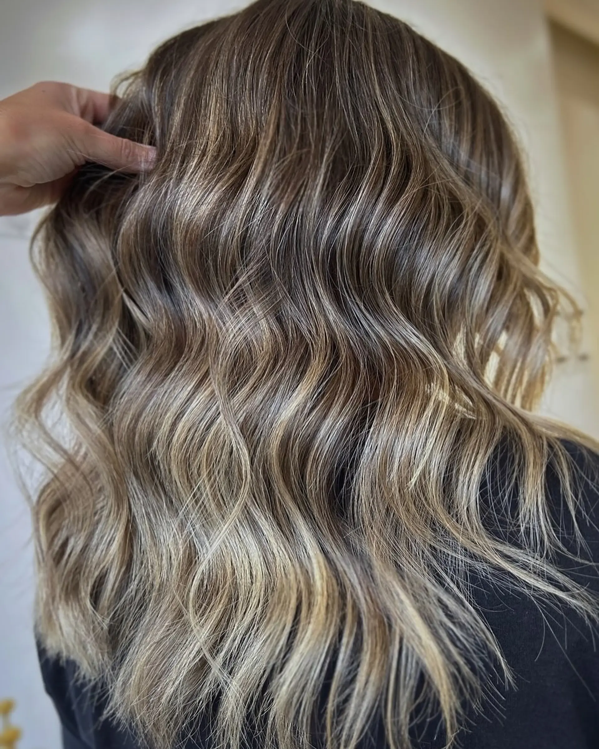 Long hair styled into loose, flowing waves with seamless dimensional blonde highlights blended over a cool brunette base. 1