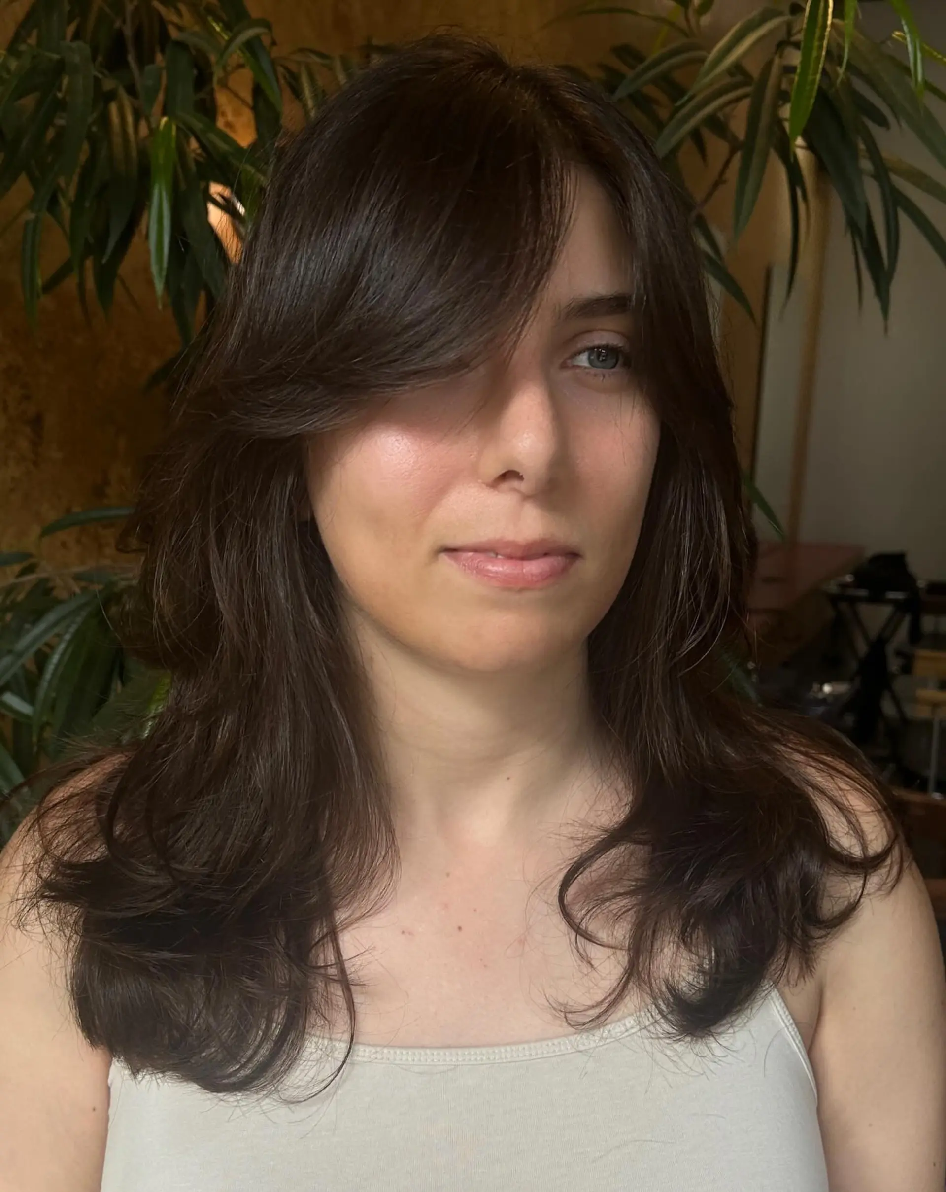 Long dark brown hair styled with face-framing layers, side-swept curtain bangs, and soft, flared ends. 1