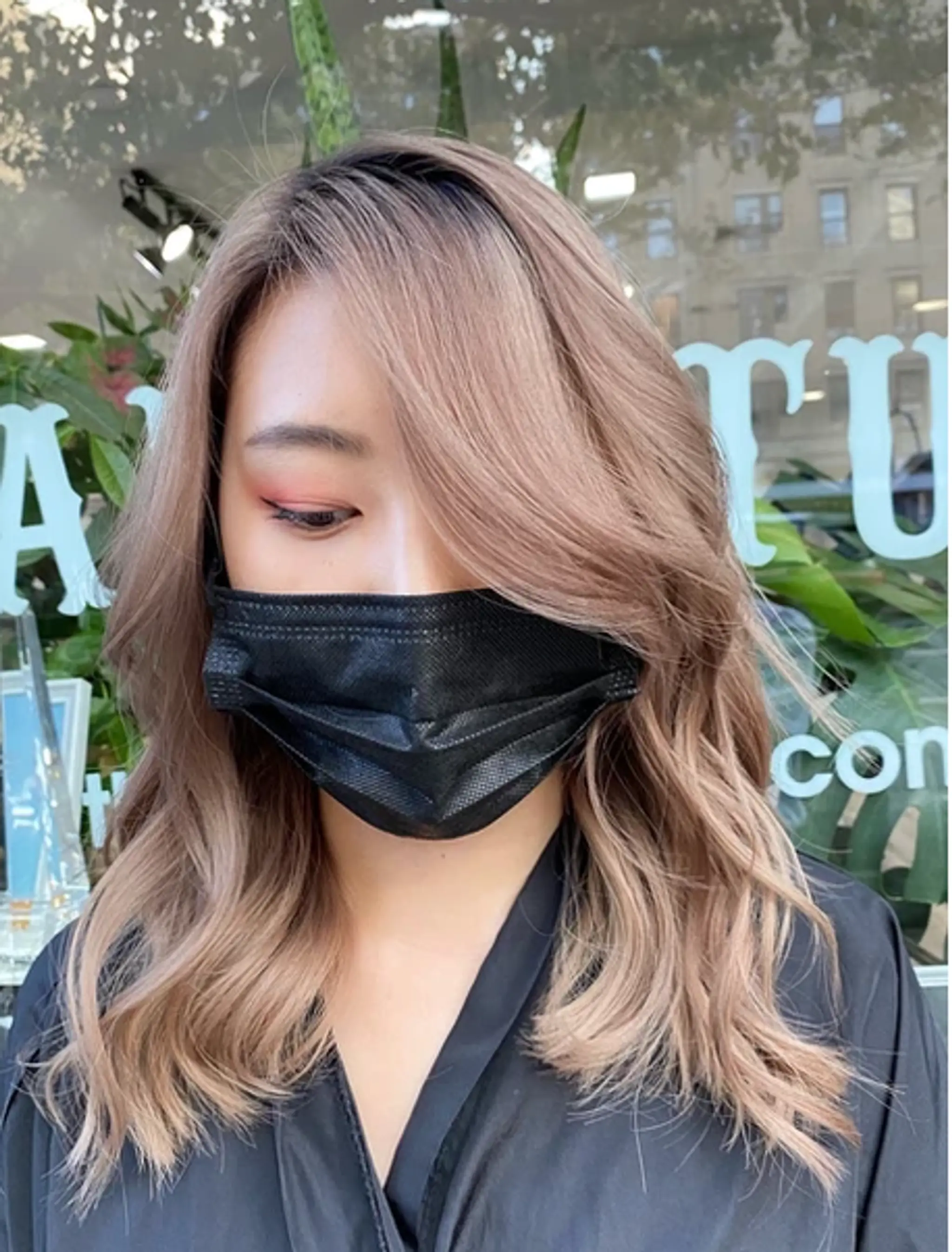 A medium-length, wavy hairstyle in champagne blonde, featuring side-swept bangs and layered, loose waves, providing a soft, flowing look with a shiny finish.
