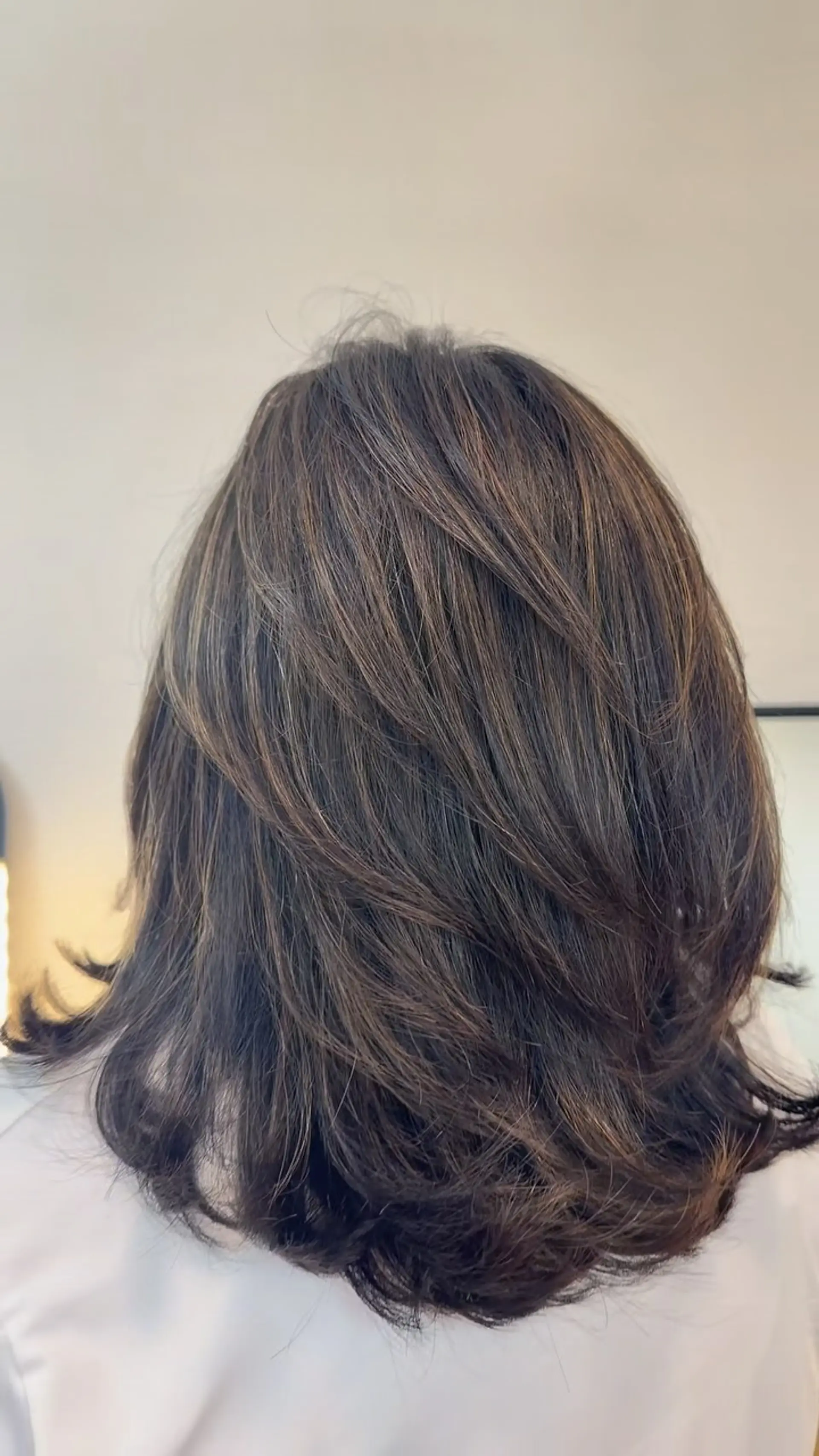 A medium-length textured layered haircut featuring soft beige-brown balayage highlights styled with curved ends. 1