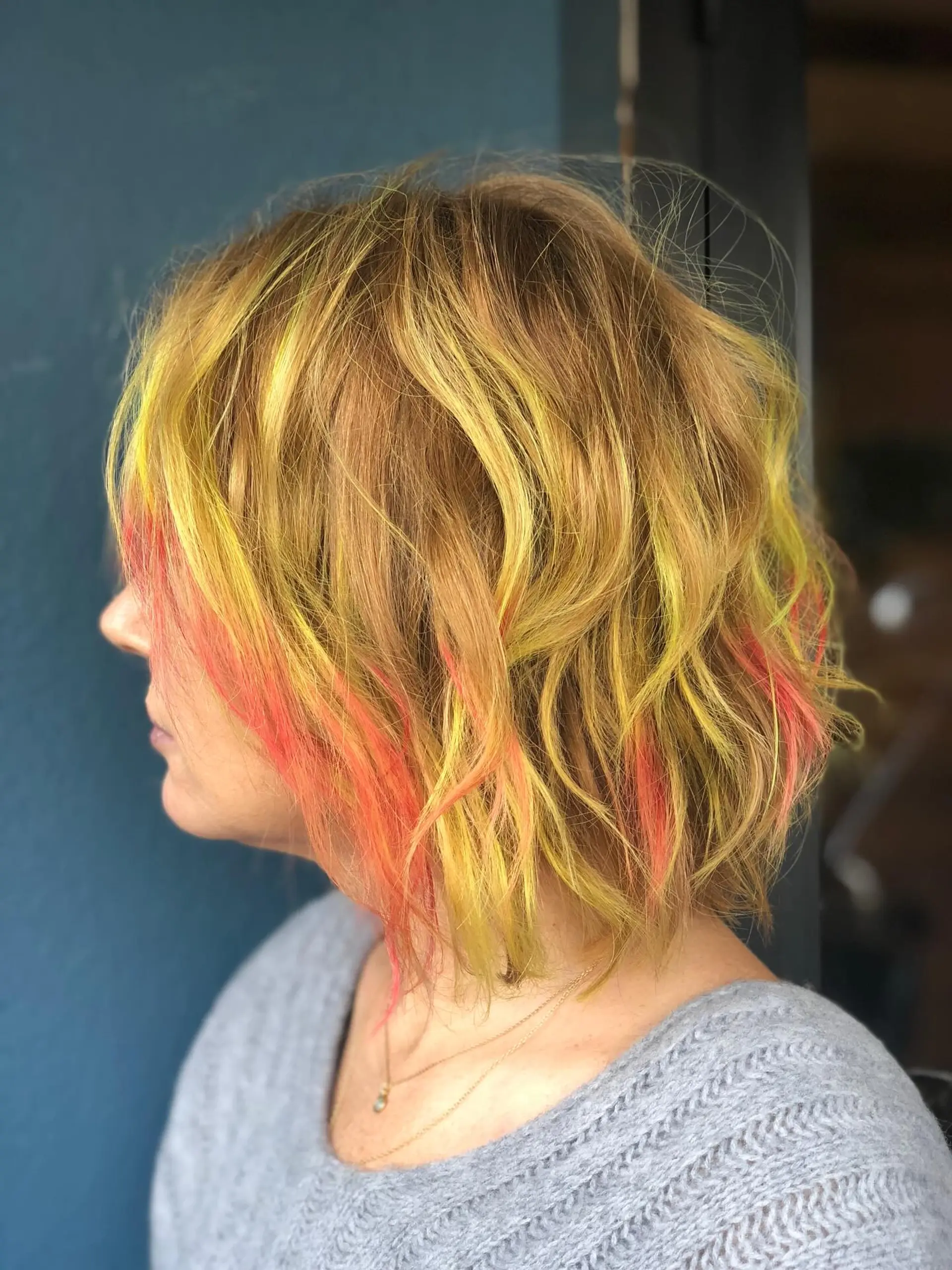 A textured wavy bob styled with undone bends, featuring a warm honey-toned base with bright neon yellow and coral pink accent streaks. Current Cut My Hair service: $215 for haircut and included finish only; displayed color is not included. 1