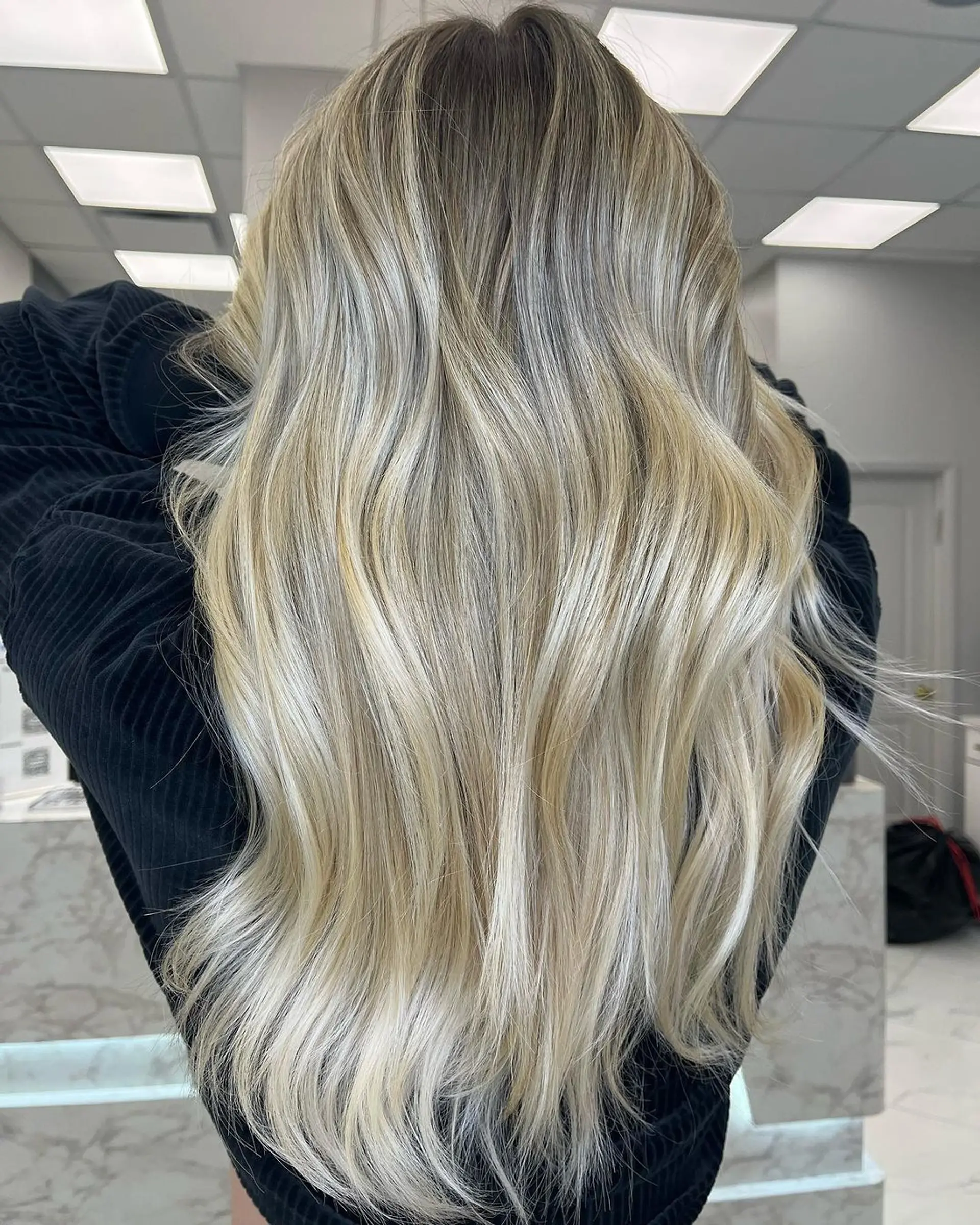 Long, wavy hair with an ash brown root shadow and blonde balayage, featuring layered, soft waves for a natural look. 1