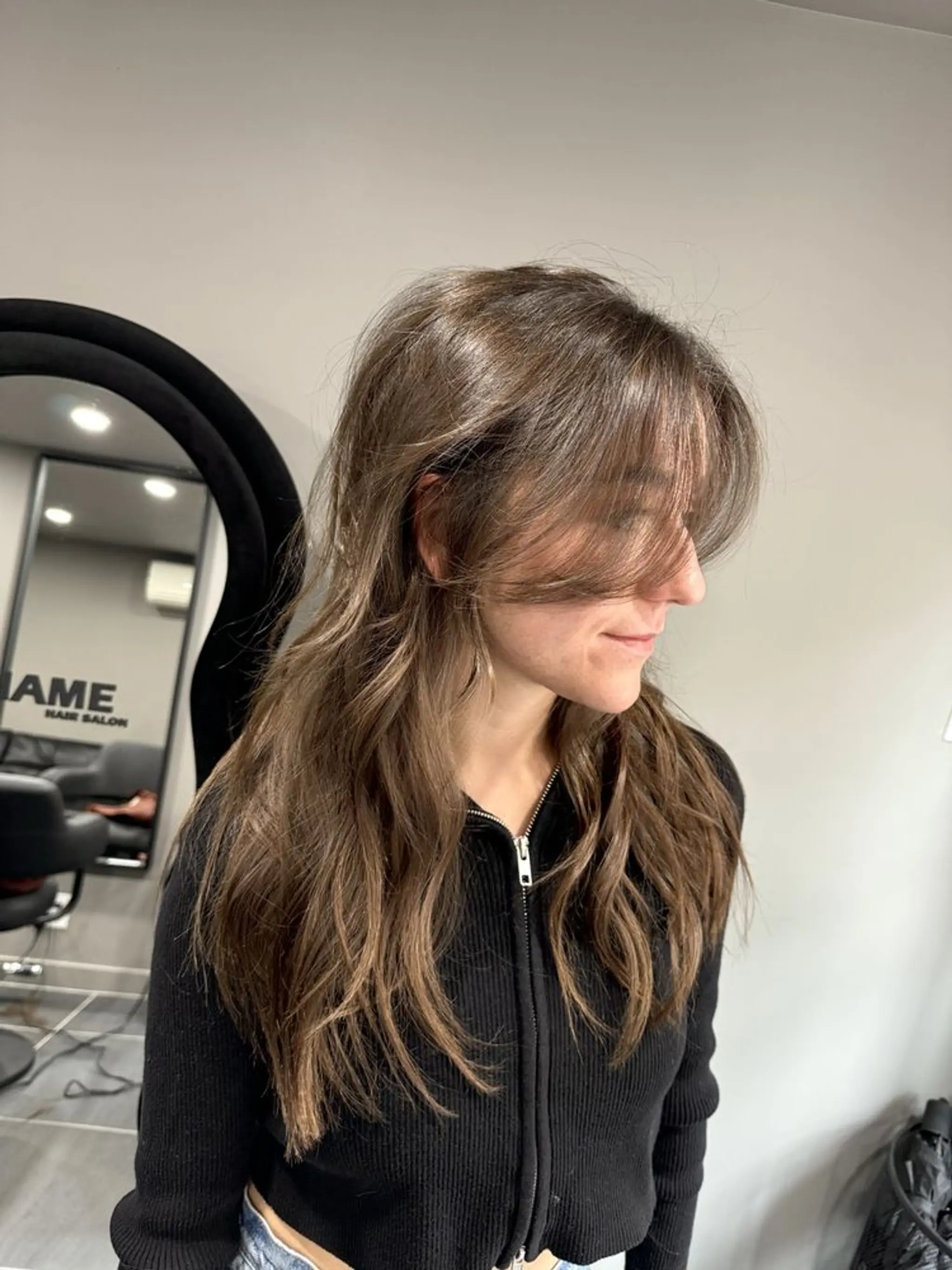 Gentle, flowing waves cascading from layers with an elegant, soft fringe that frames the face, adding dimension and movement. The layers add volume and texture for an effortlessly styled look.