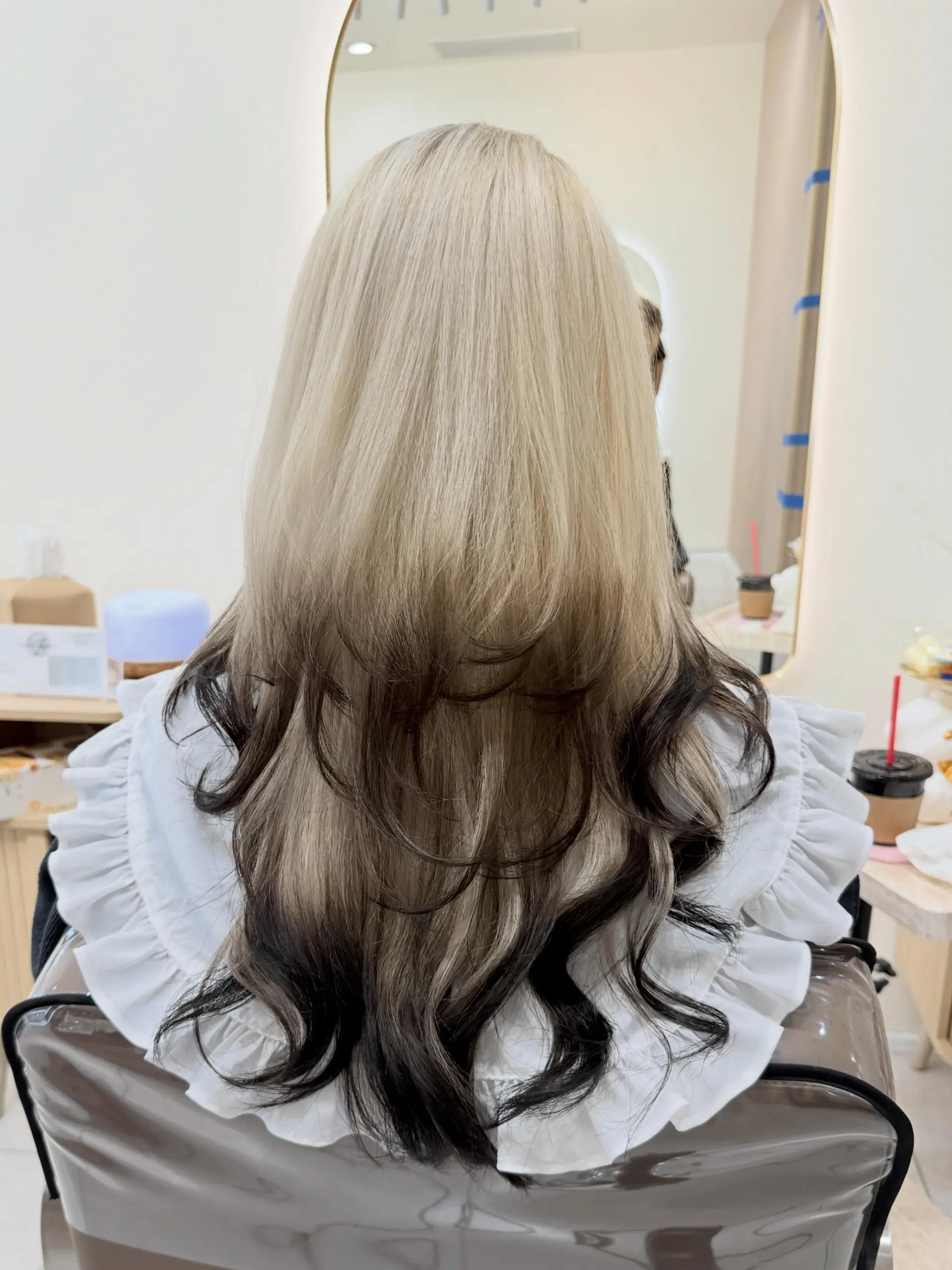 Long platinum blonde hair cut into textured layers with contrasting deep black color at the mid-lengths and ends styled in soft curls. 1