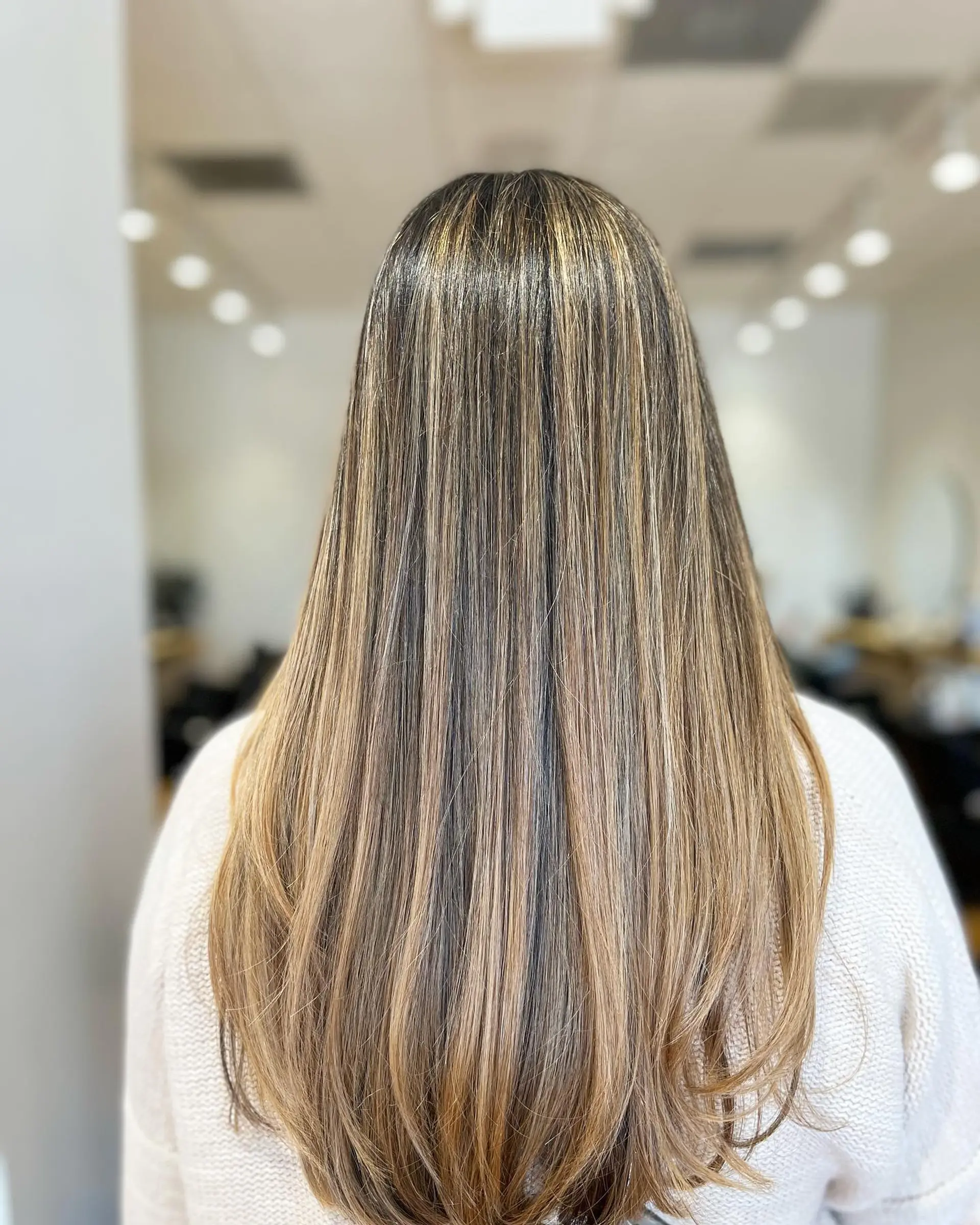 Long, sleek straight hair detailed with seamless warm blonde highlights integrated into a natural brunette base, finished with a smooth blowout and subtly curved ends. 1