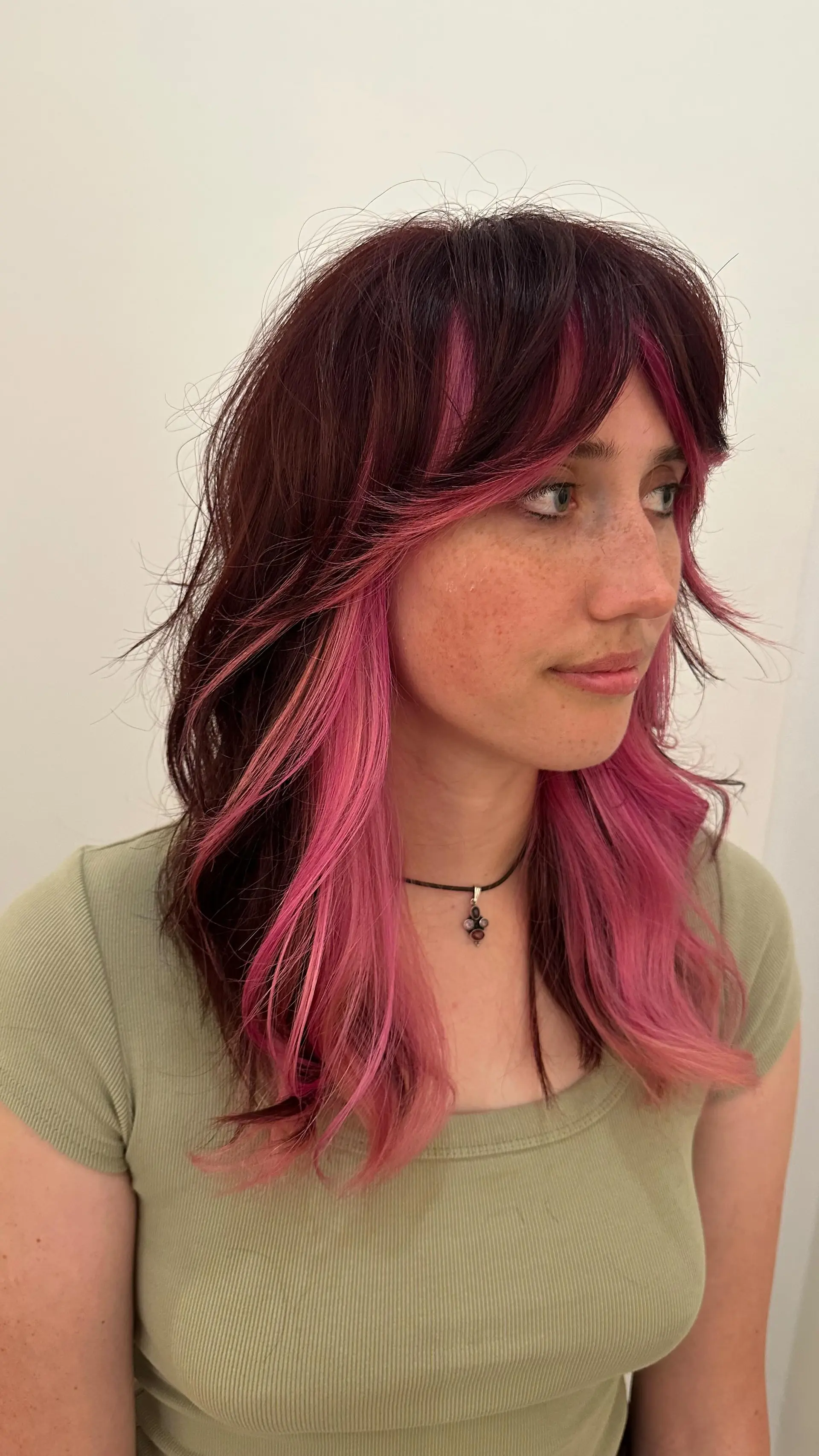 Medium-length shag with curtain bangs featuring vibrant pink peekaboo color blocking beneath dark brown layers. 1