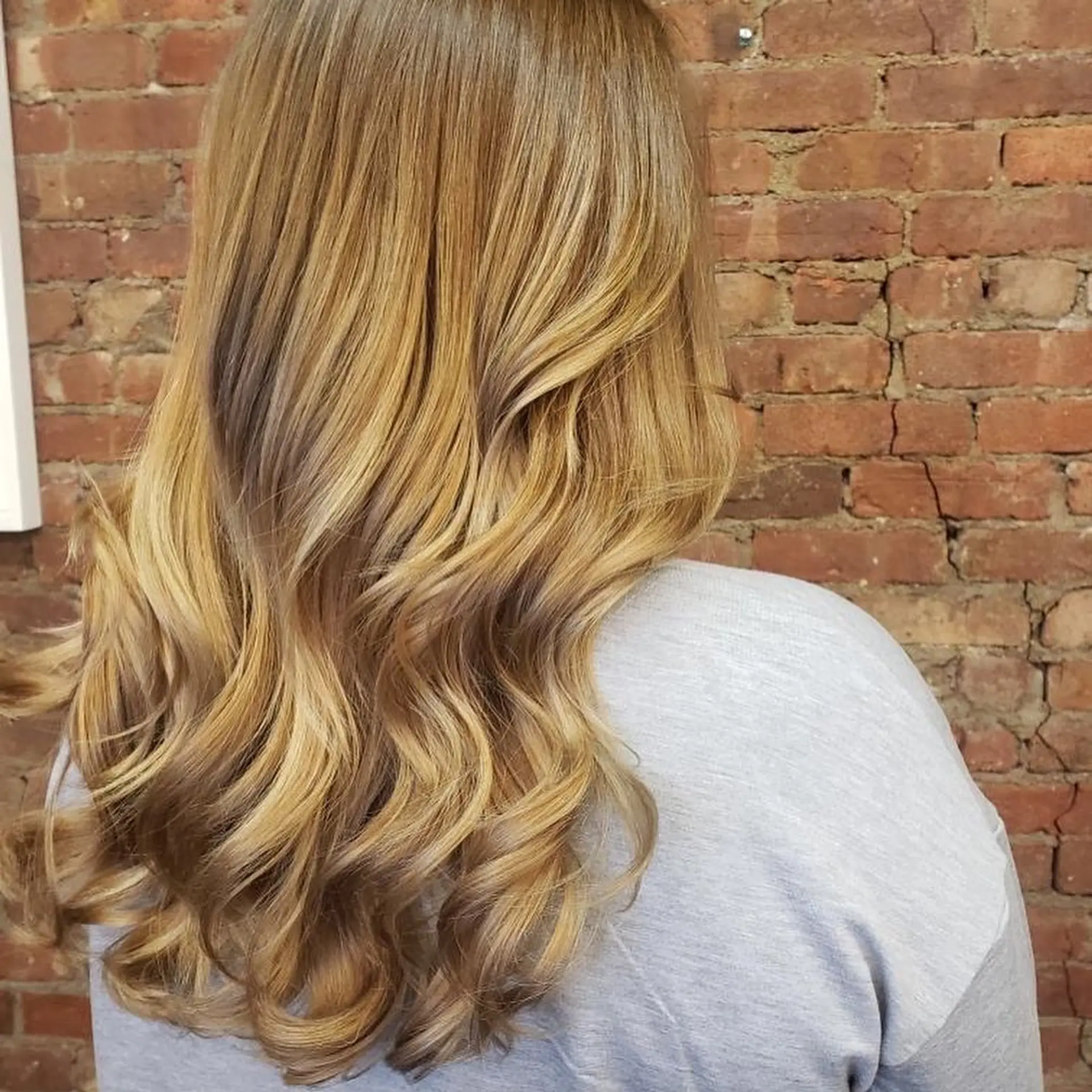 Long honey blonde hair featuring seamless dimensional balayage highlights styled in soft curls. 1