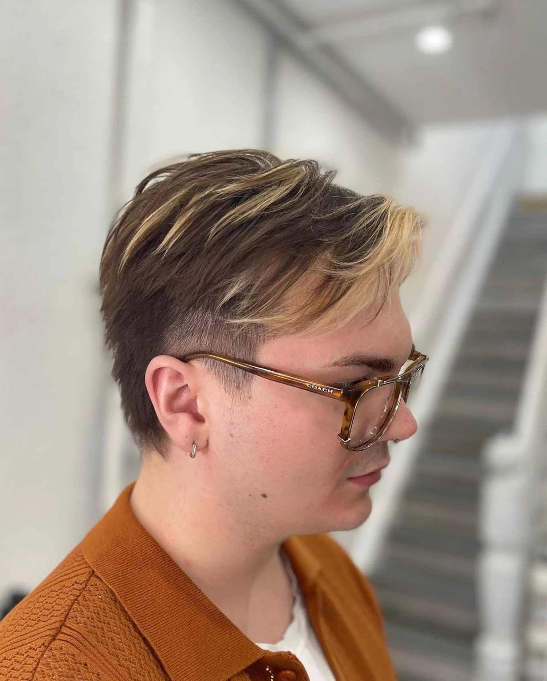 A short, layered hairstyle with a two-tone color scheme of blonde and brown, featuring an undercut and fade with voluminous blonde strands on top. 1