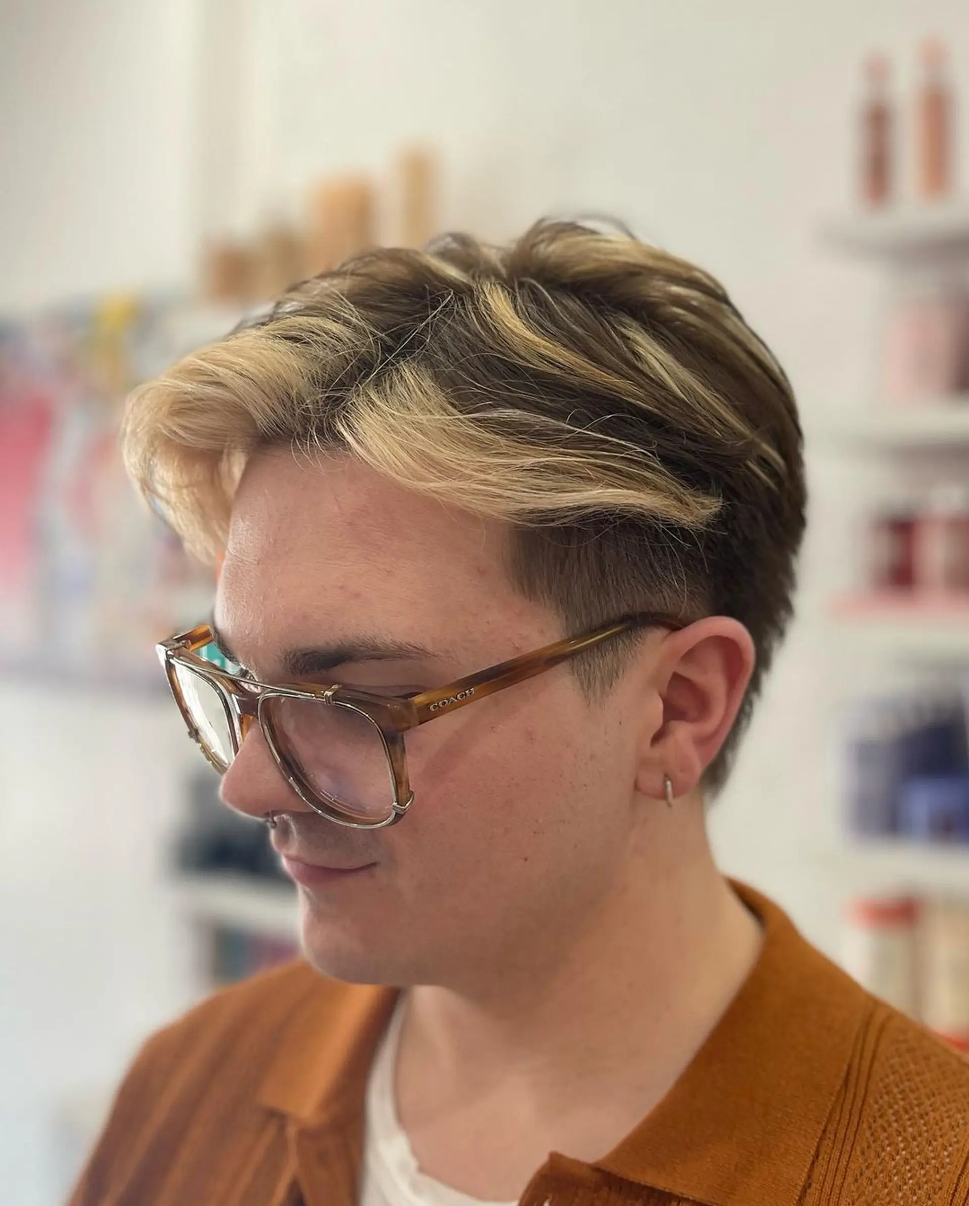 A short, layered hairstyle with a two-tone color scheme of blonde and brown, featuring an undercut and fade with voluminous blonde strands on top. 2
