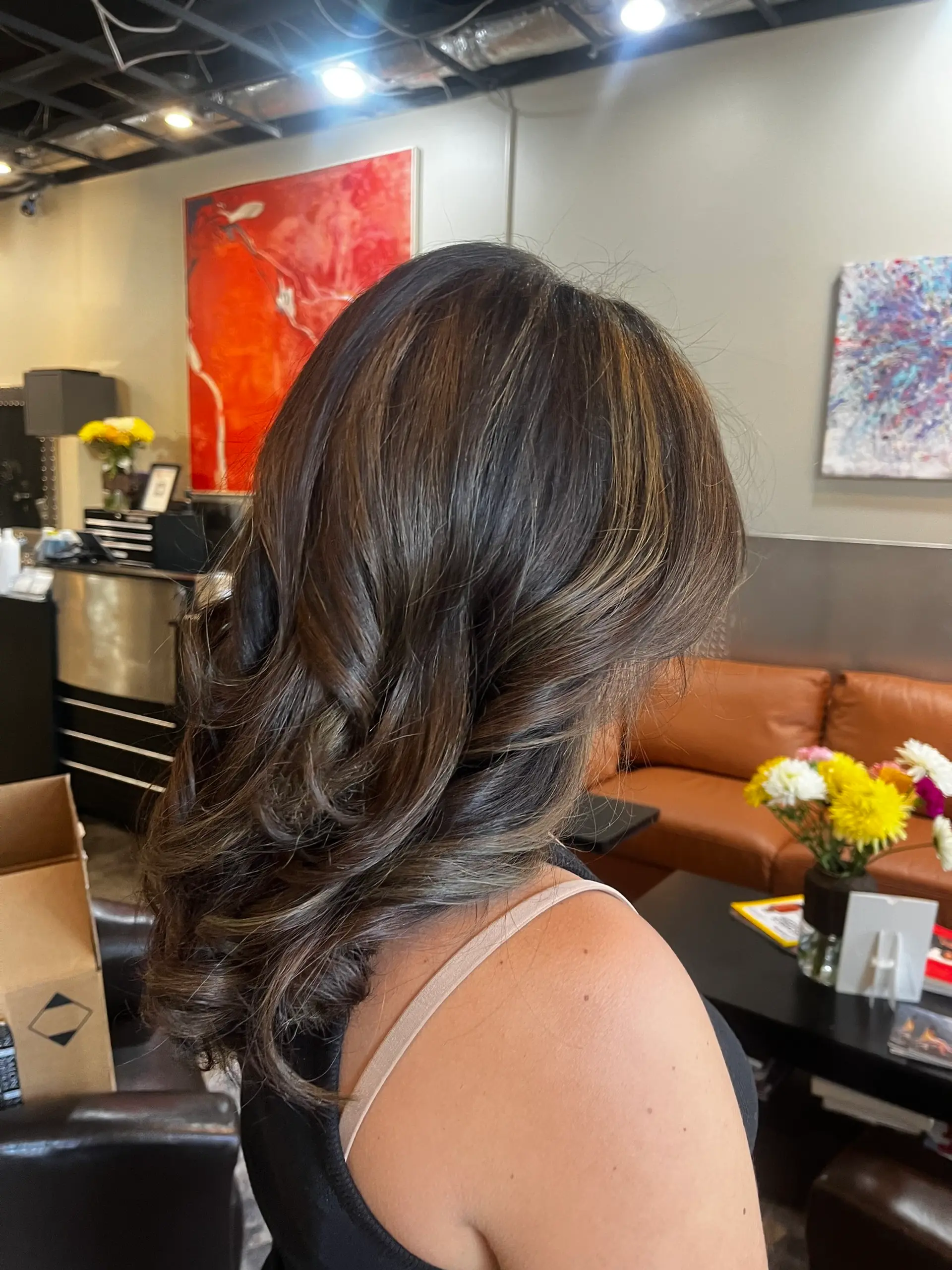 Medium-length dark brown hair styled with soft, voluminous curls and subtle warm caramel highlights. 1