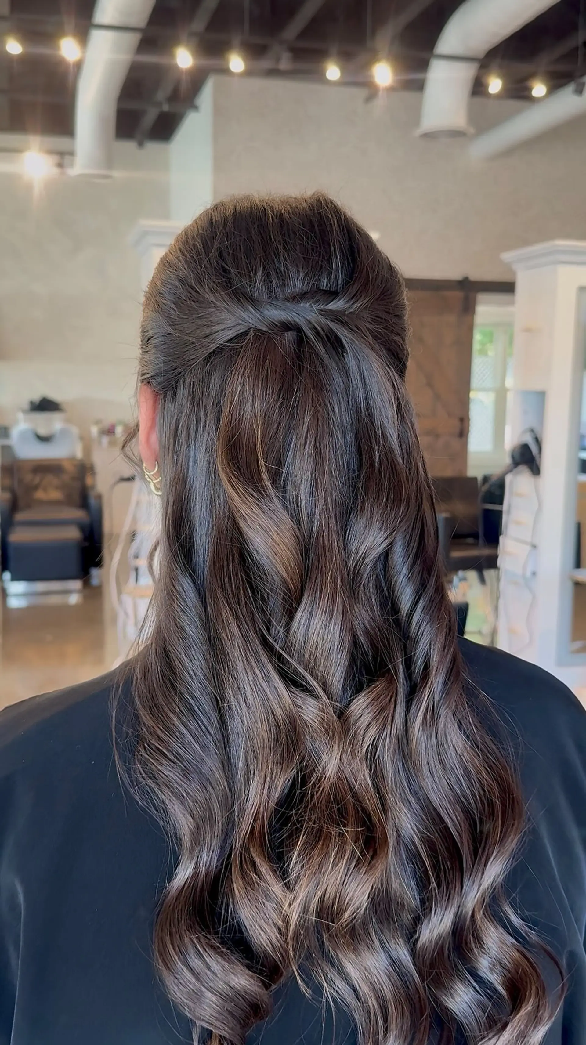 A sleek half-up style featuring a soft twist at the crown flowing down into cascading, loose polished waves. 1
