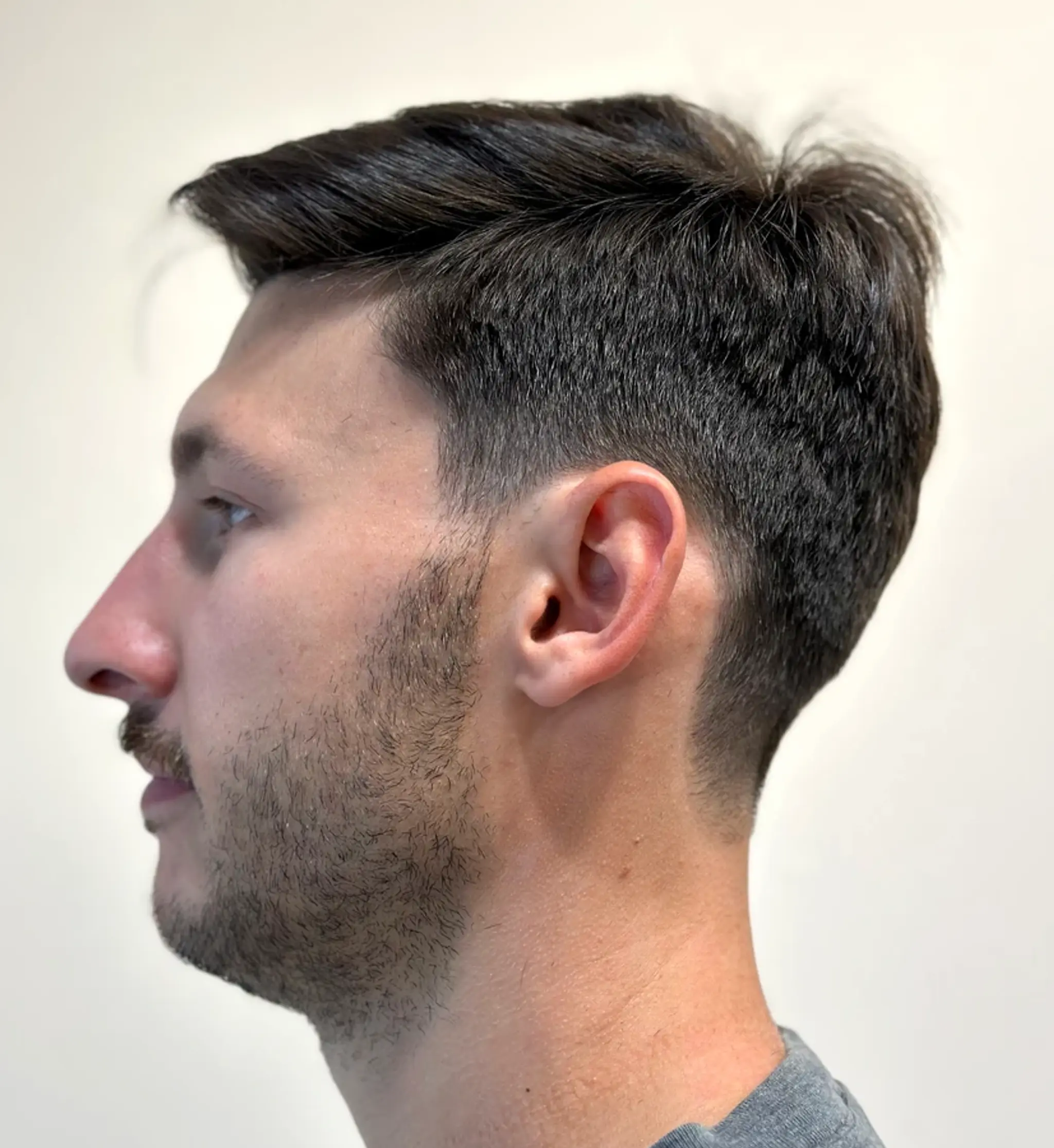 The hairstyle features a sleek side-swept appearance with a sharp taper fade along the sides and back, with straight and textured hair on top.