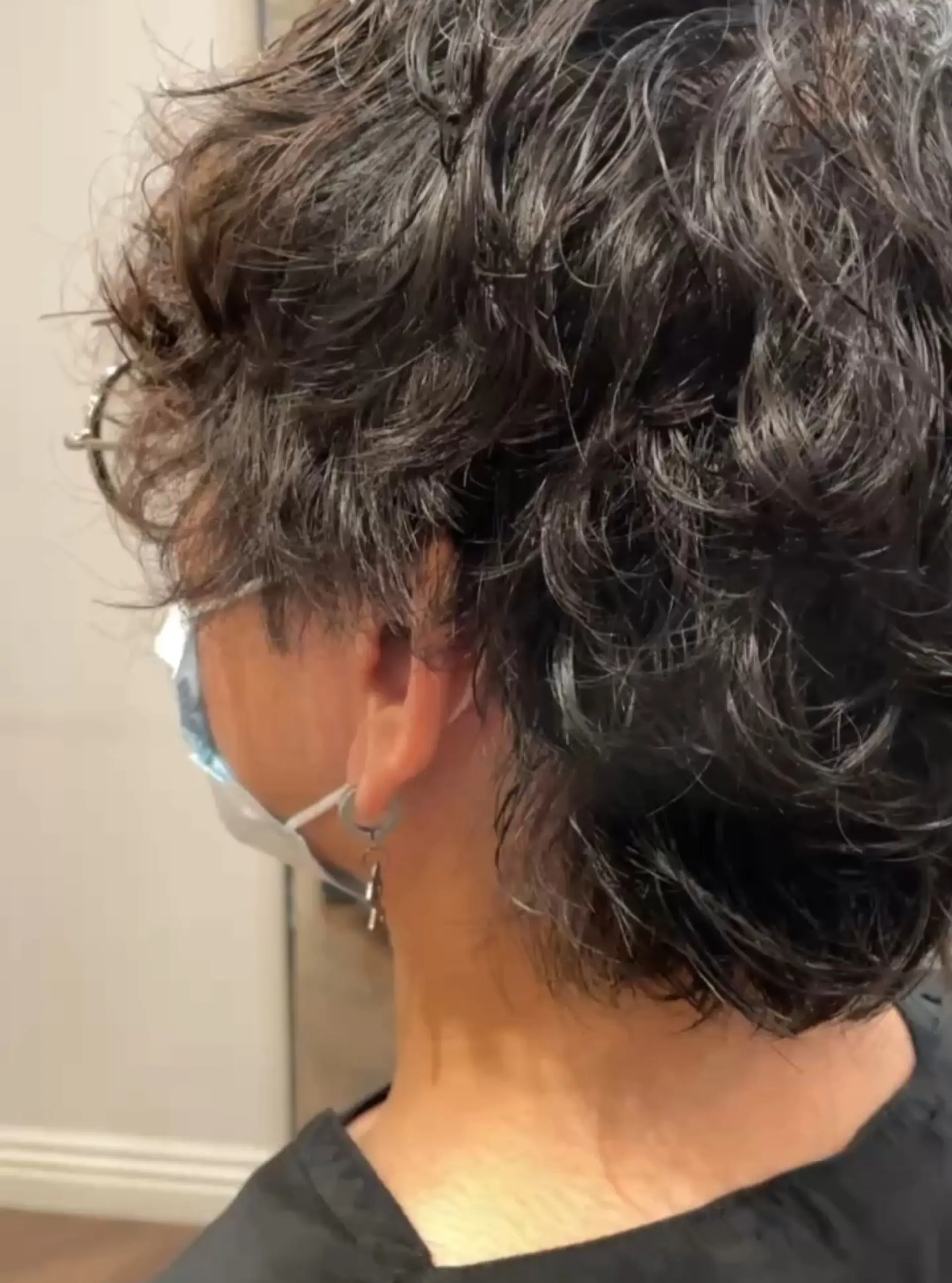 A men's short haircut styled with a soft perm to create natural wavy texture, volume, and effortless movement. 1