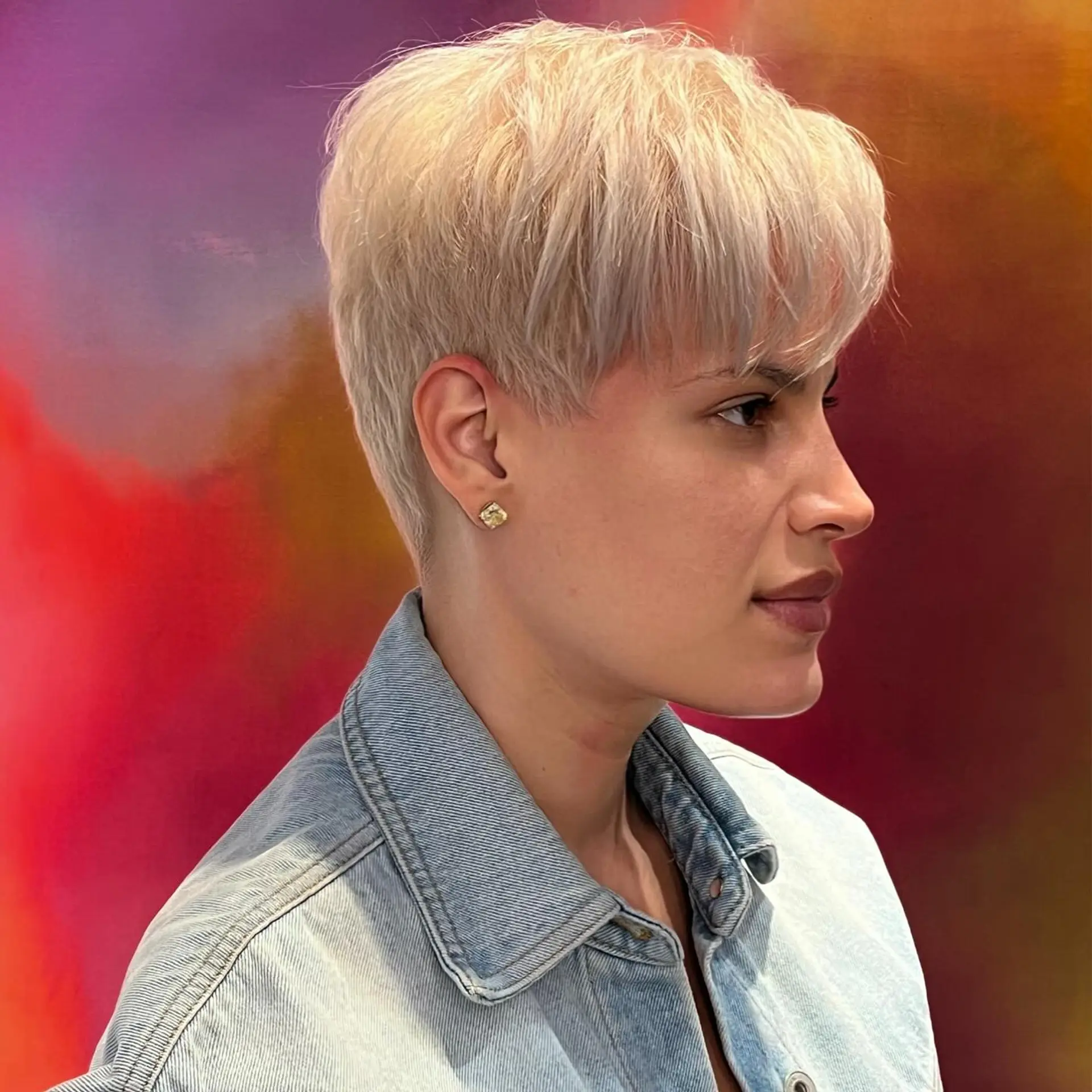 A soft, textured platinum blonde pixie cut styled forward with wispy bangs and neat tapered sides. 1
