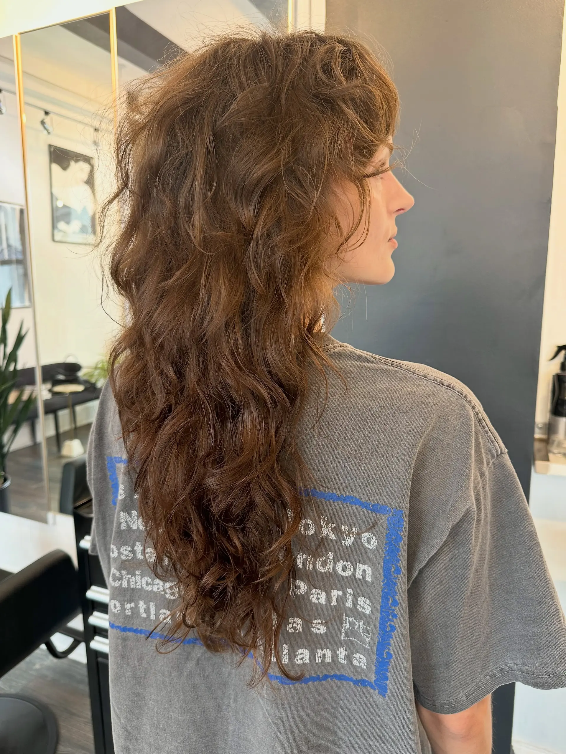 A long textured brunette shag haircut with defined natural waves, layered crown volume, and wispy bangs. 1