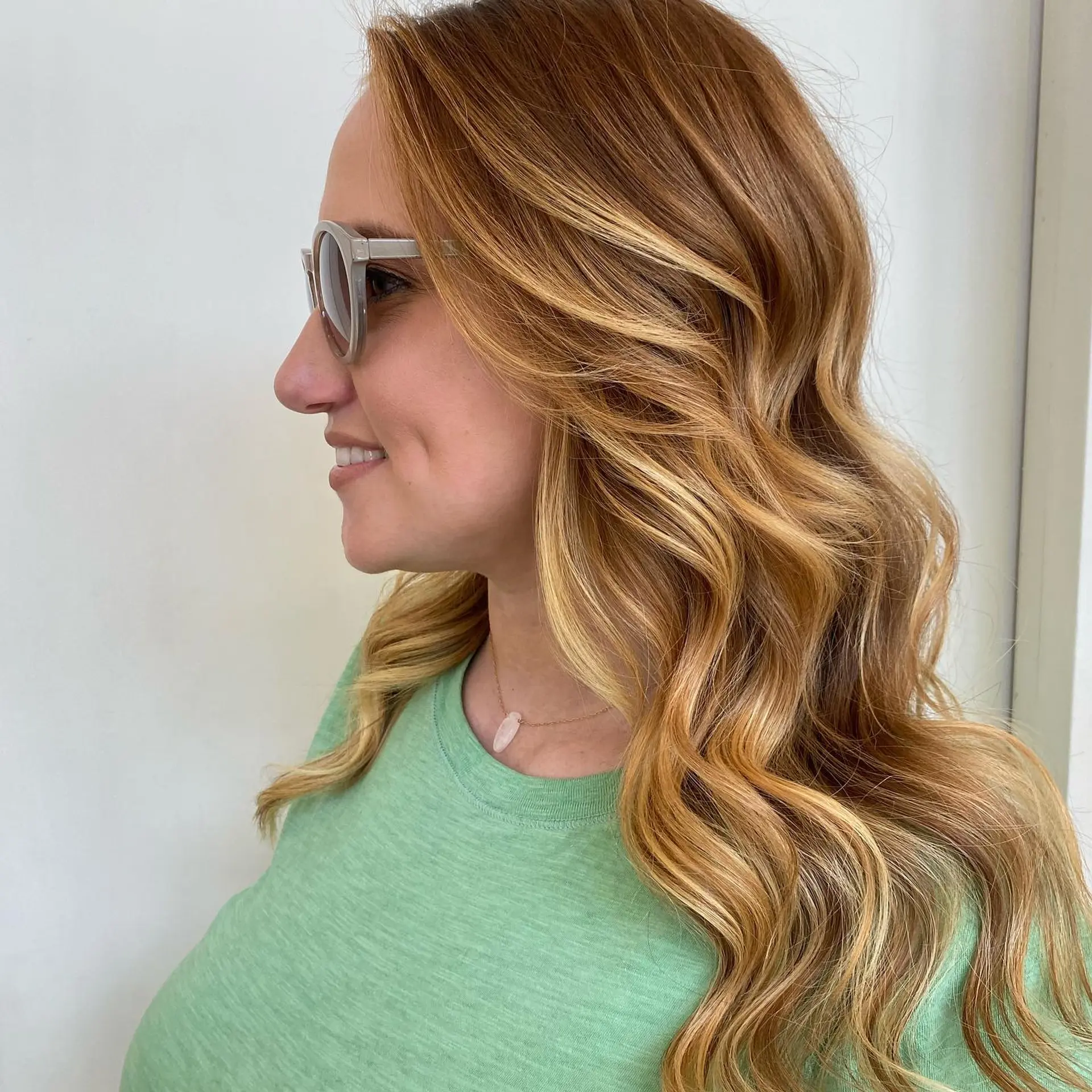 Long strawberry blonde hair styled with soft, cascading waves and seamless golden highlights. 1
