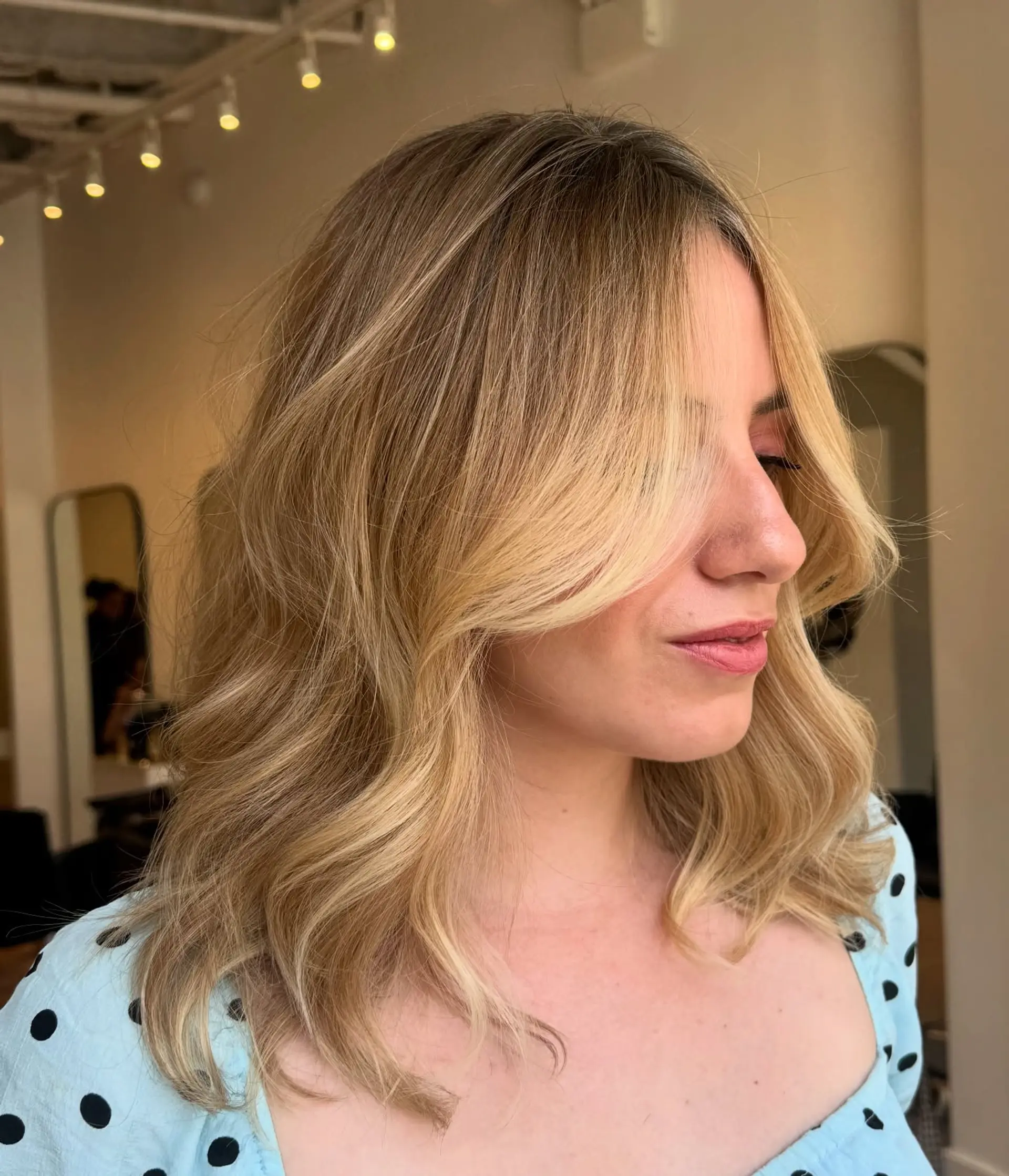 Medium-length layered blonde hair styled in soft waves with long curtain bangs framing the face. 1