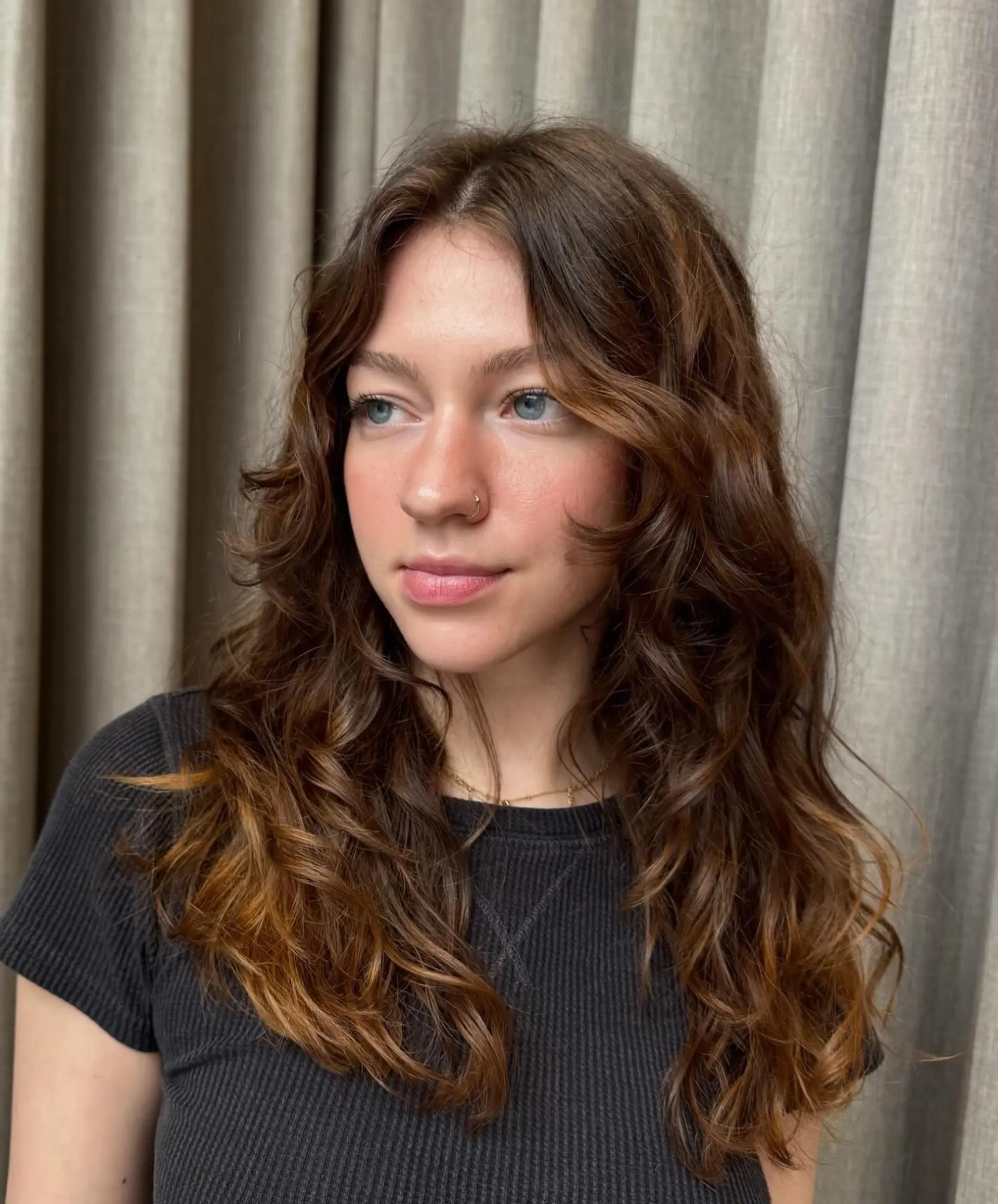 Long wavy layered haircut featuring curtain bangs and subtle warm brown highlights. 1