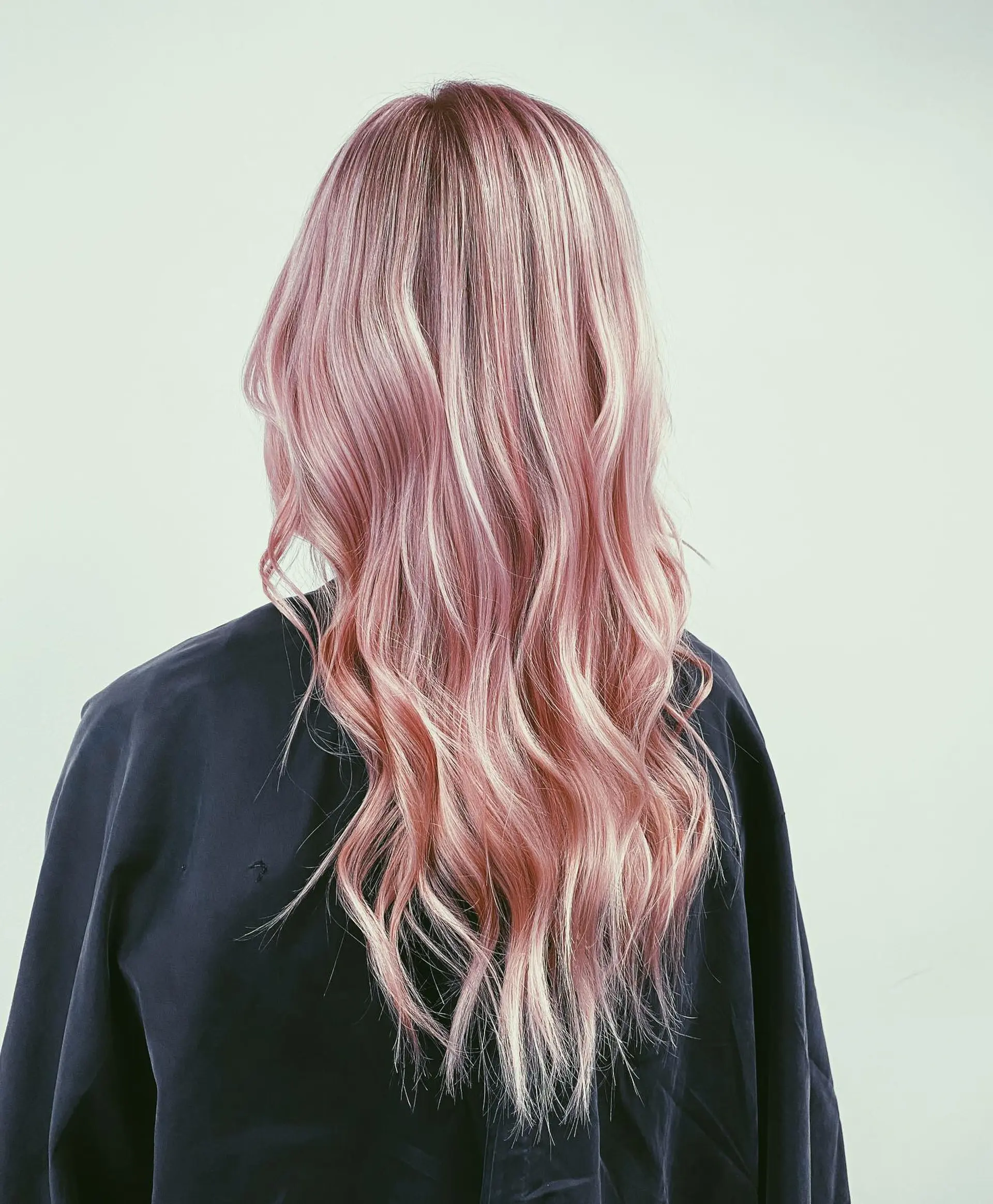 Long wavy hair styled with loose bends featuring a dimensional pastel pink and blonde balayage. 1