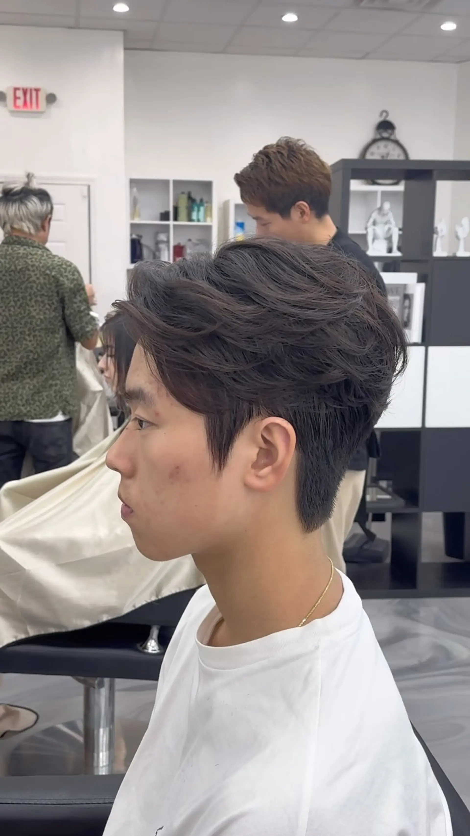 A modern men's two-block haircut featuring soft, textured layers swept back on top with clean tapered sides. 1