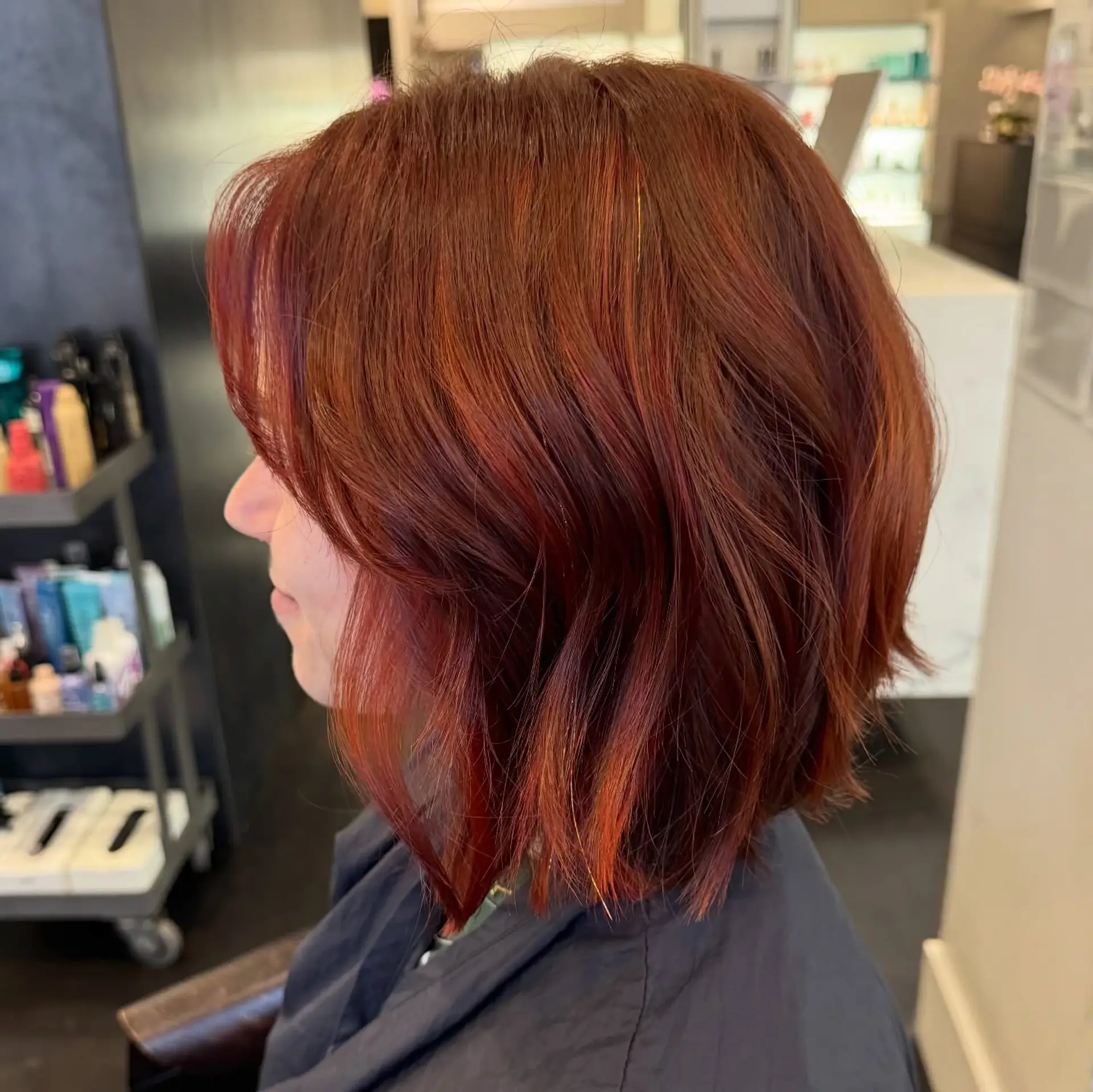 A textured neck-length bob cut styled with soft, piecey bends in a warm auburn red color. 1