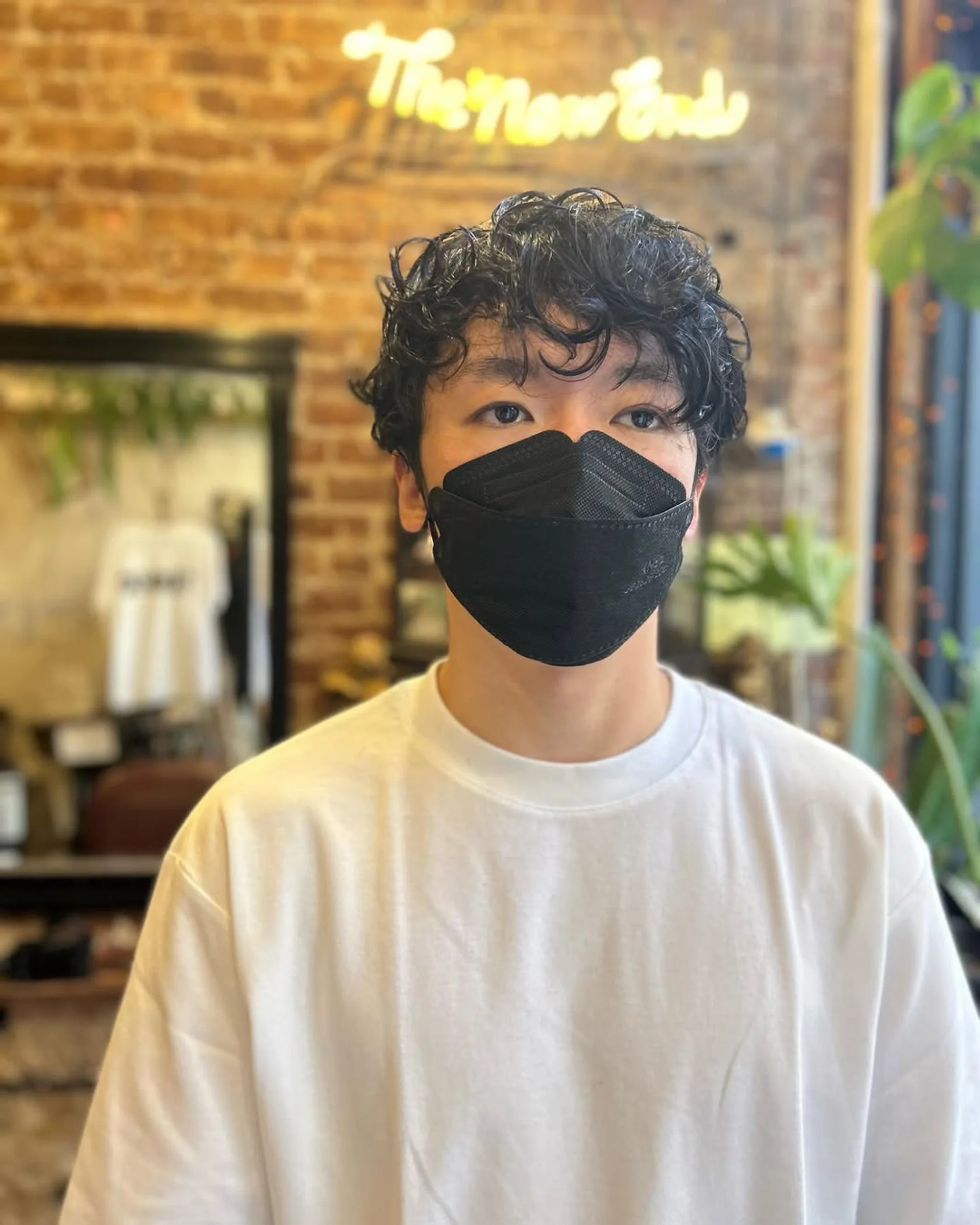 A model showcasing the 2026 men's curl trend: a textured crop with highly defined curls and faded sides, seen in a modern NYC salon. - Preview 1
