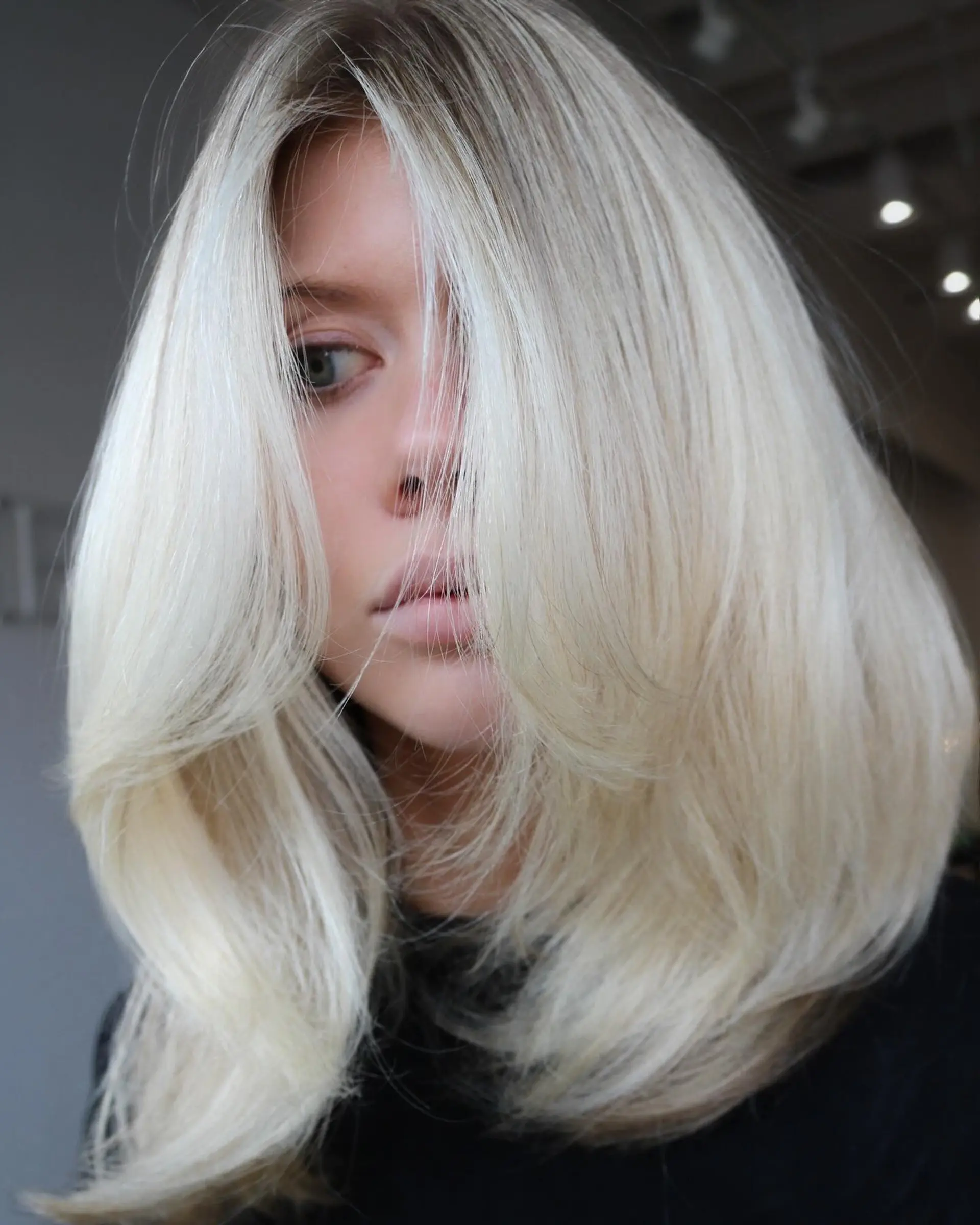 A bright neutral blonde medium-length haircut featuring voluminous face-framing layers and a polished blowout finish. 1