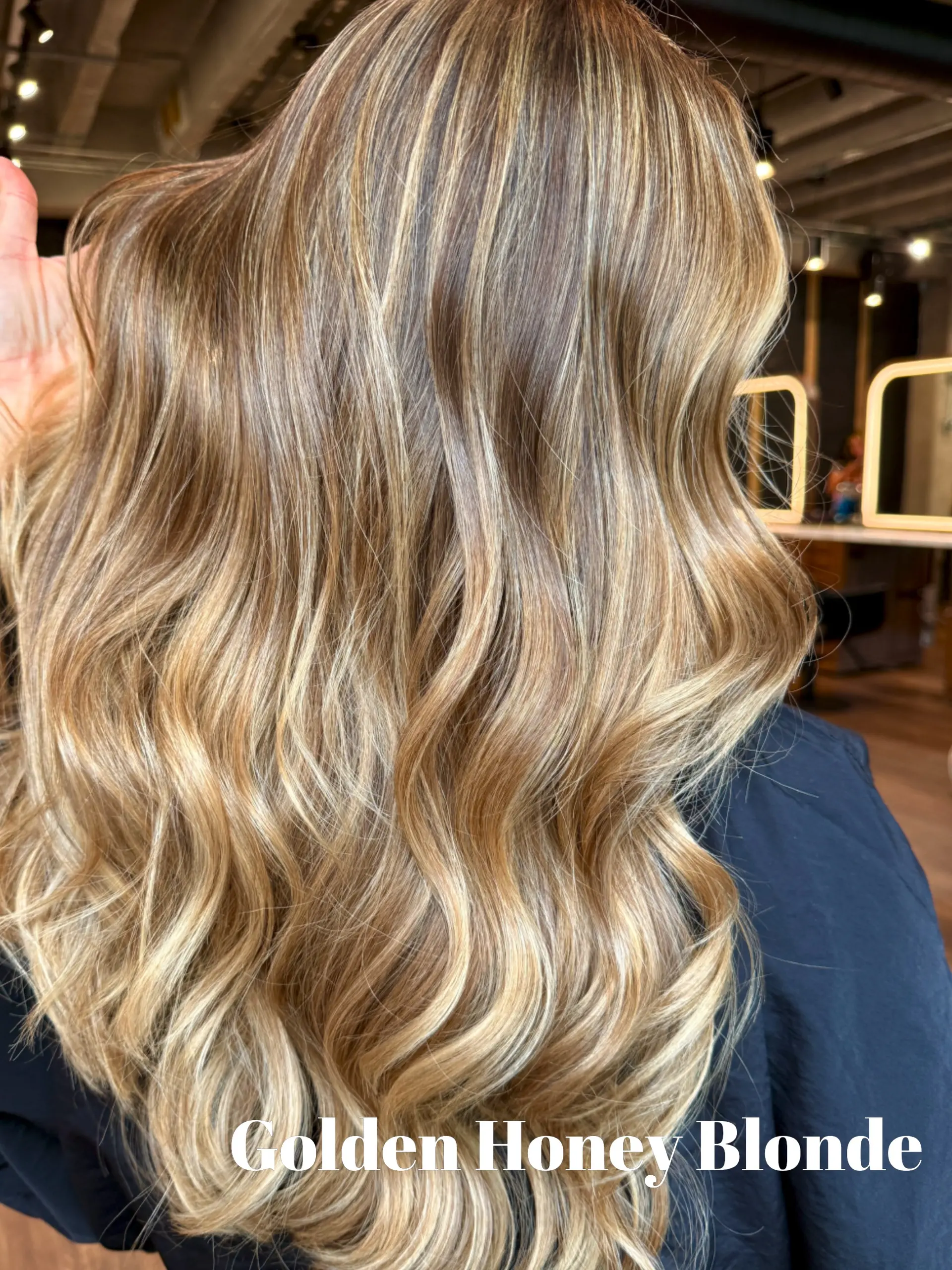Long hair colored in warm golden honey blonde tones and styled into loose, shiny waves. 1
