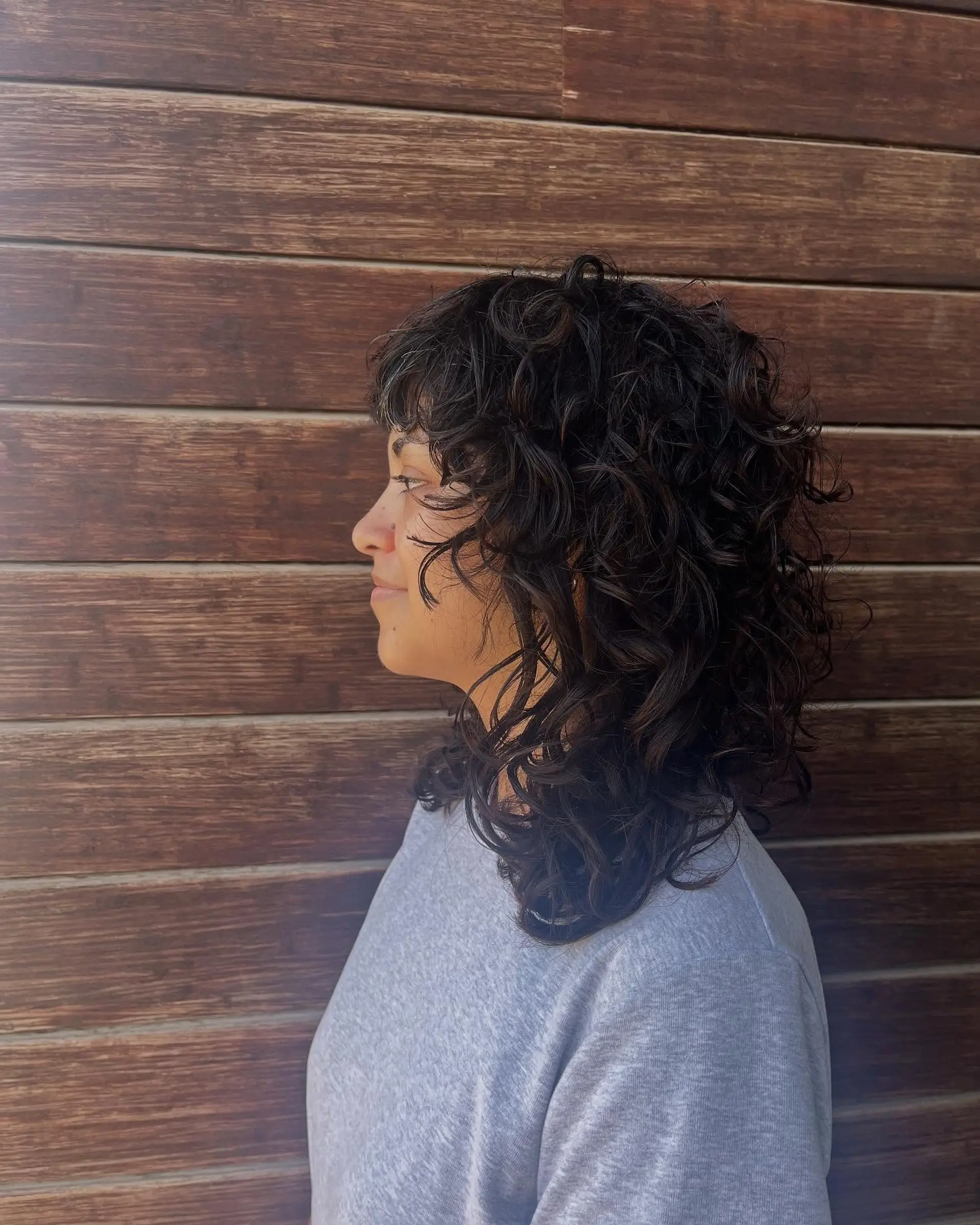 A medium-length dark curly shag cut featuring soft, textured layers and curly bangs framing the face. 1