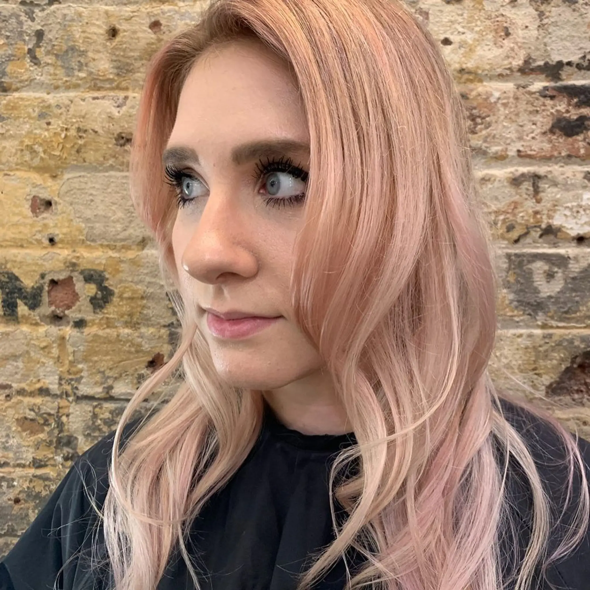 Long, rose gold wavy hair with a side part and soft layers, featuring pastel pink undertones and a trendy, voluminous look. 1