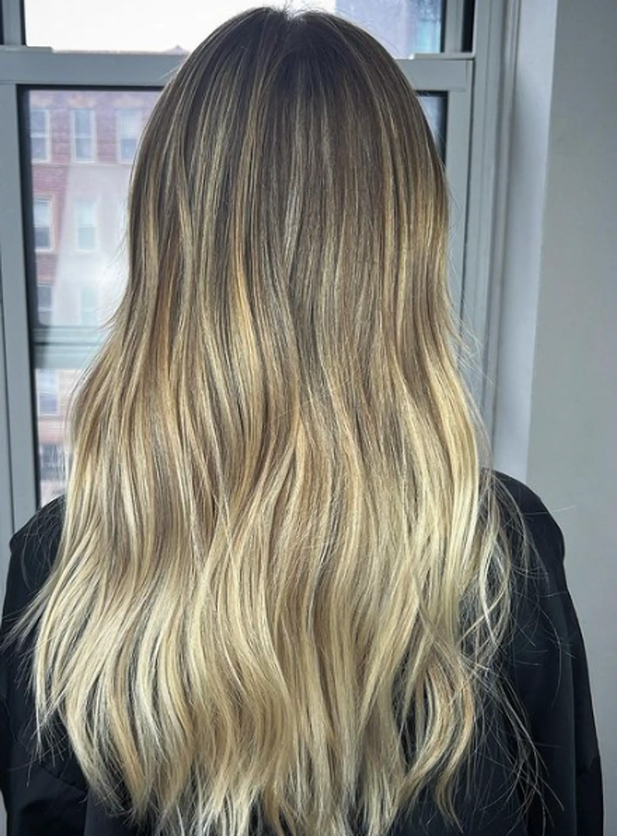 Long, wavy hair with dark brunette roots transitioning through dark blonde to light blonde ends, featuring an ombre and balayage effect.