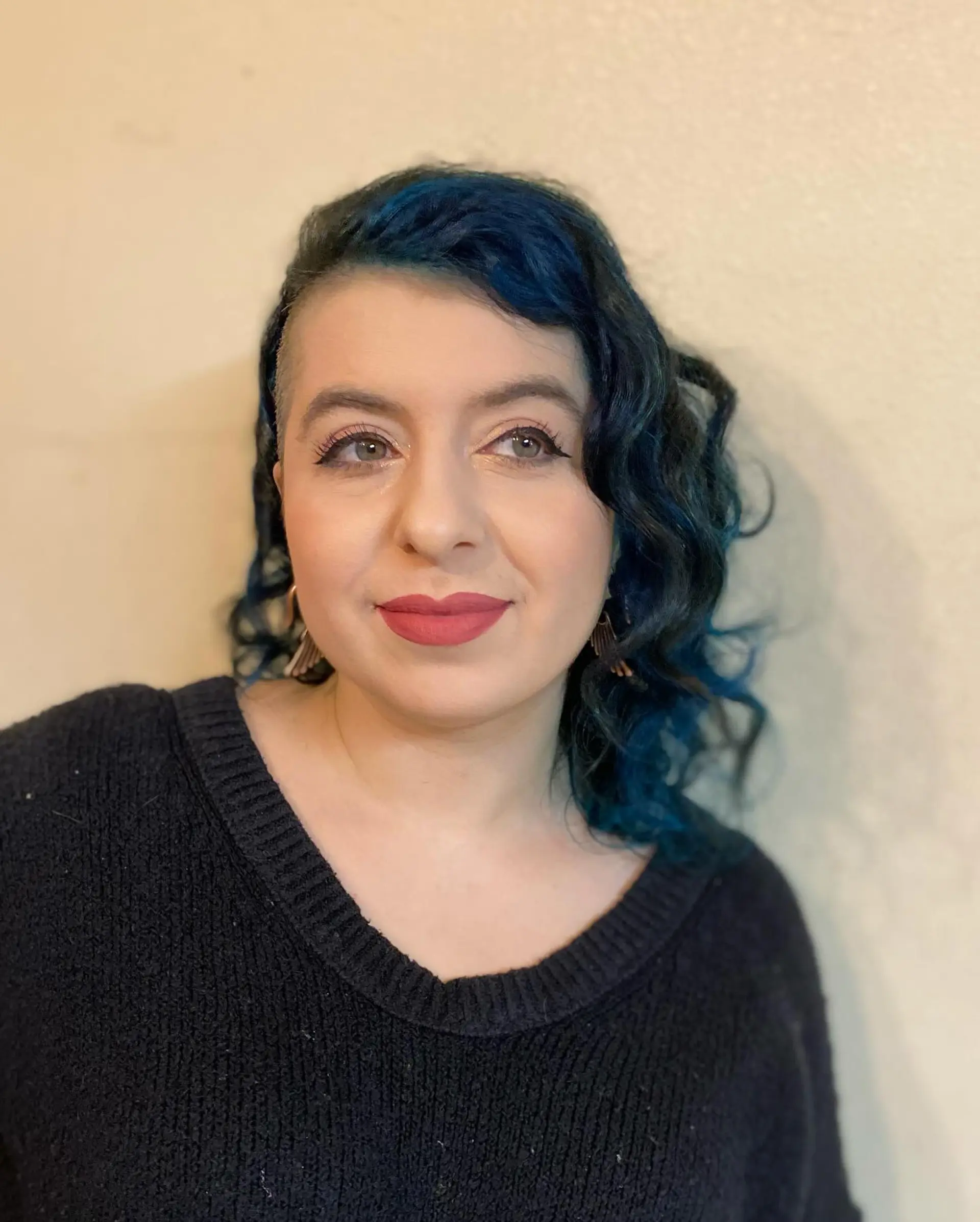 Medium-length wavy dark hair featuring chunky vibrant blue highlights and a shaved sidecut. 1