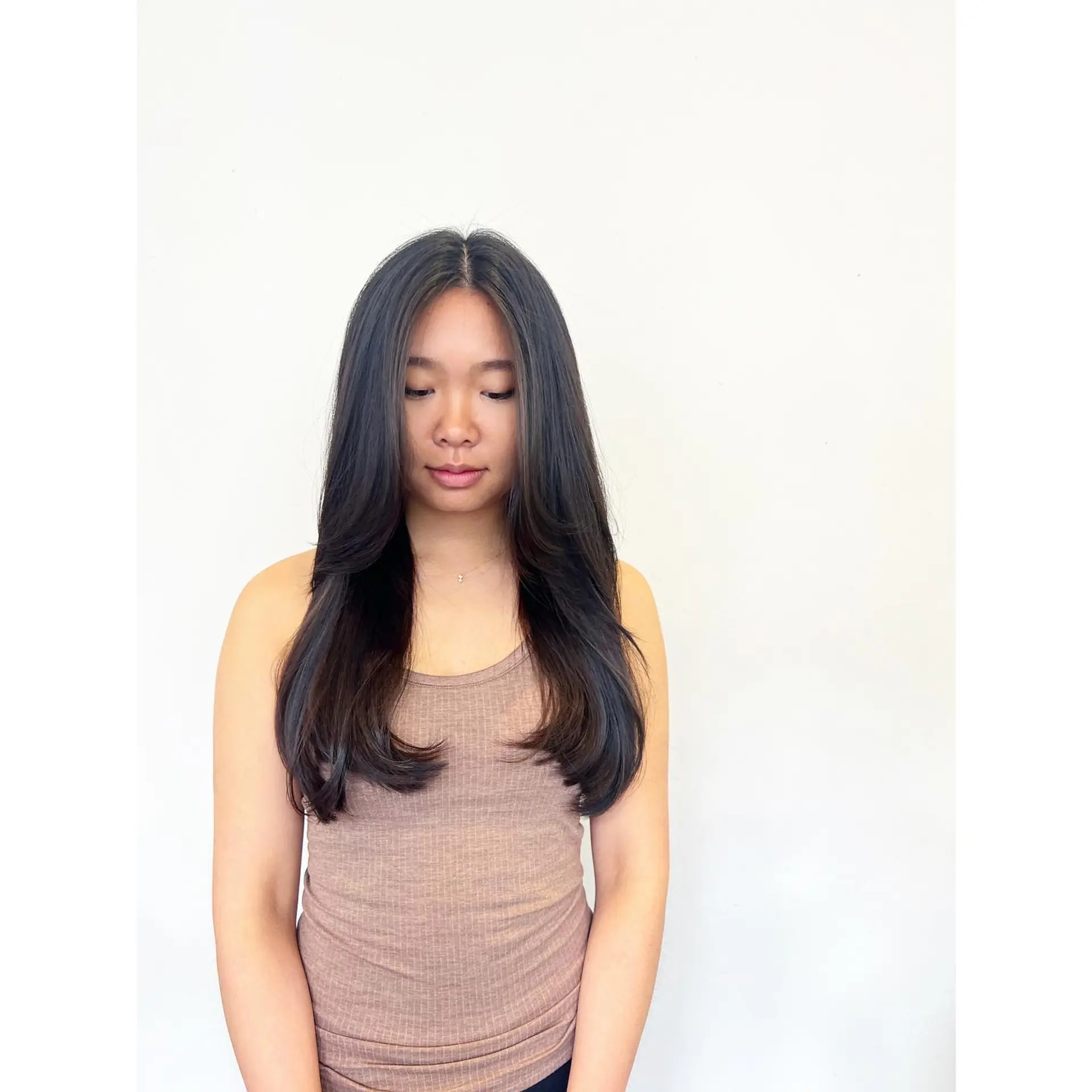 Smooth long dark hair styled with face-framing layers and soft, curved-in ends. 1