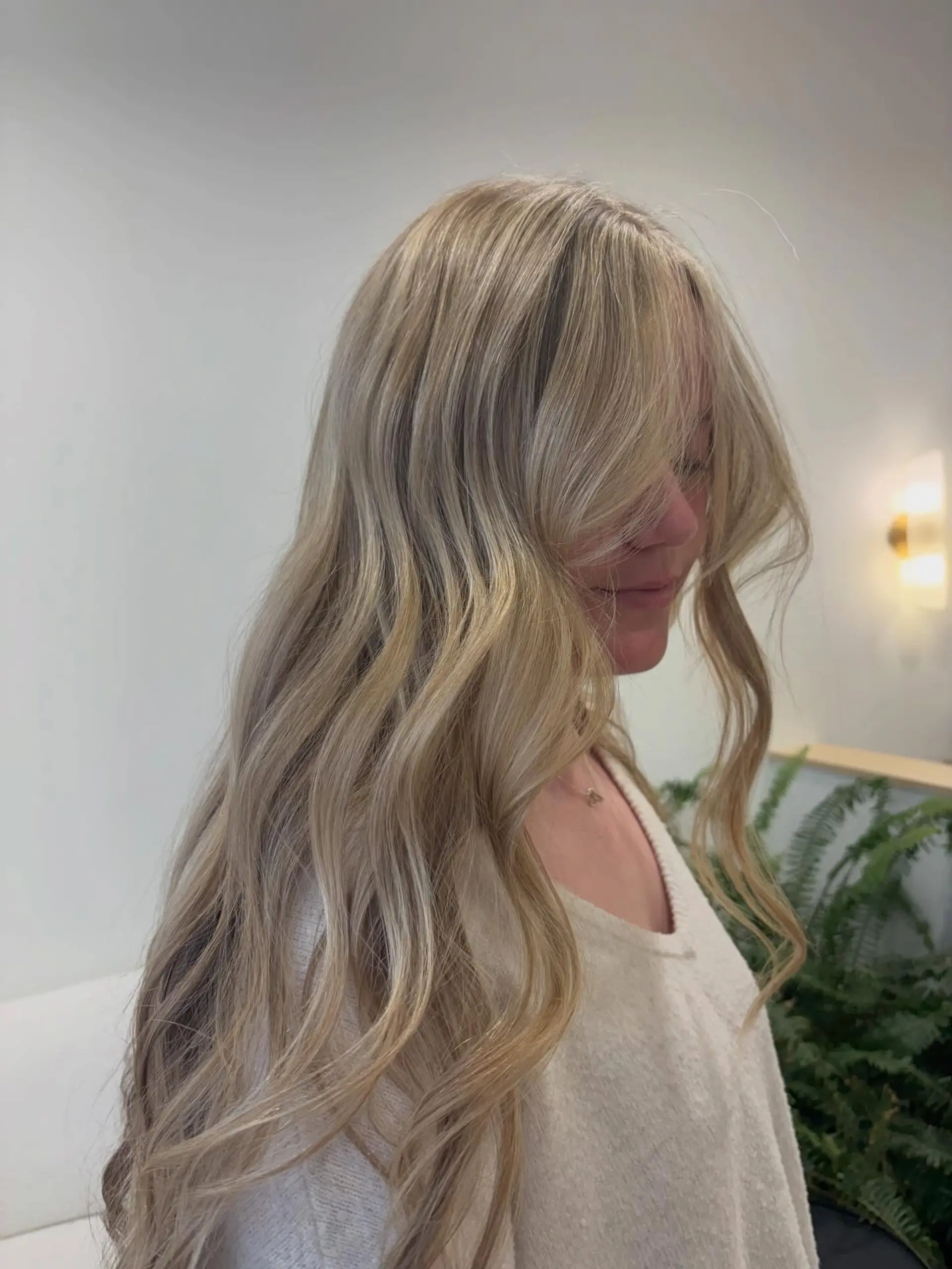Long dimensional blonde hair styled in loose, flowing waves with textured curtain bangs framing the face. 1