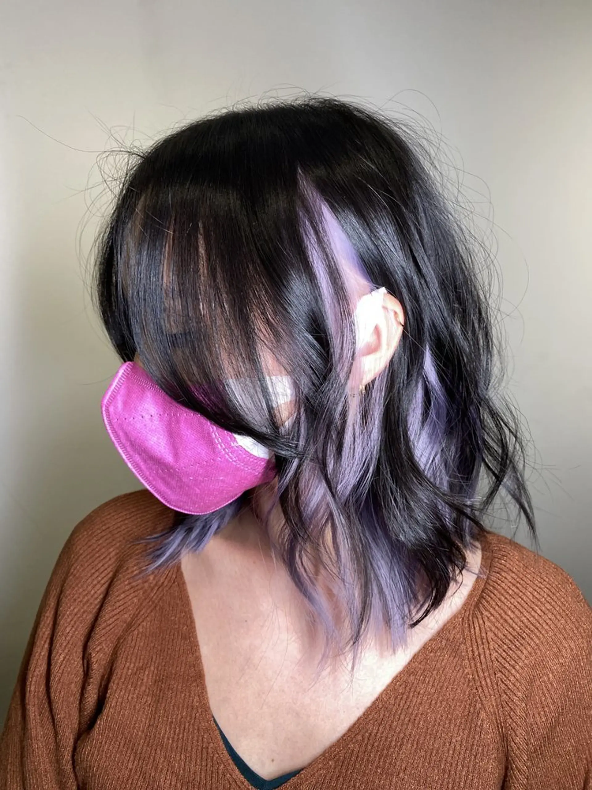 Medium-length, wavy hair with a deep black base and vibrant lavender and purple highlights. Loose waves add volume and movement, and side bangs gently cover the forehead, providing a casual yet edgy vibe. 1